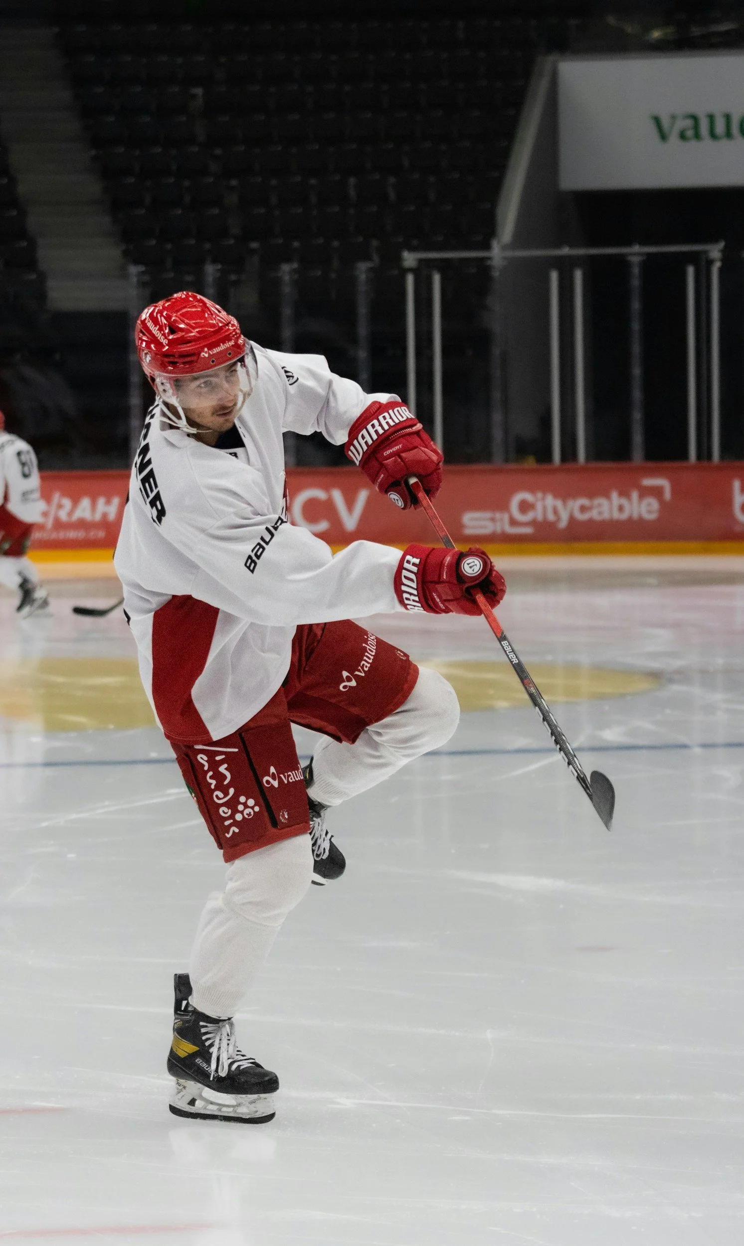 Un joueur de hockey en mouvement lors d'un entraînement ou d'un match, portant un uniforme blanc et rouge, avec un casque rouge et des gants rouges, sur la patinoire.