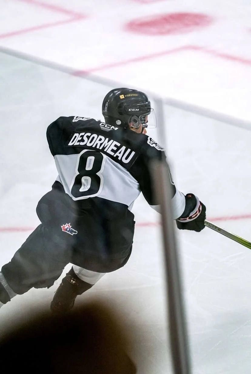Un joueur de hockey en déplacement sur la glace, portant un casque noir, un maillot noir et blanc avec le nom DESORMEAU et le numéro 8.
