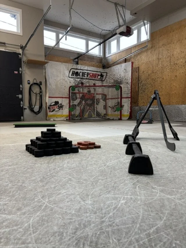 Une salle de hockey en intérieur avec une surface glacée, un but de hockey, des planches de protection, des accessoires d'entraînement, et des équipements de hockey comme des patins et des bâtons.