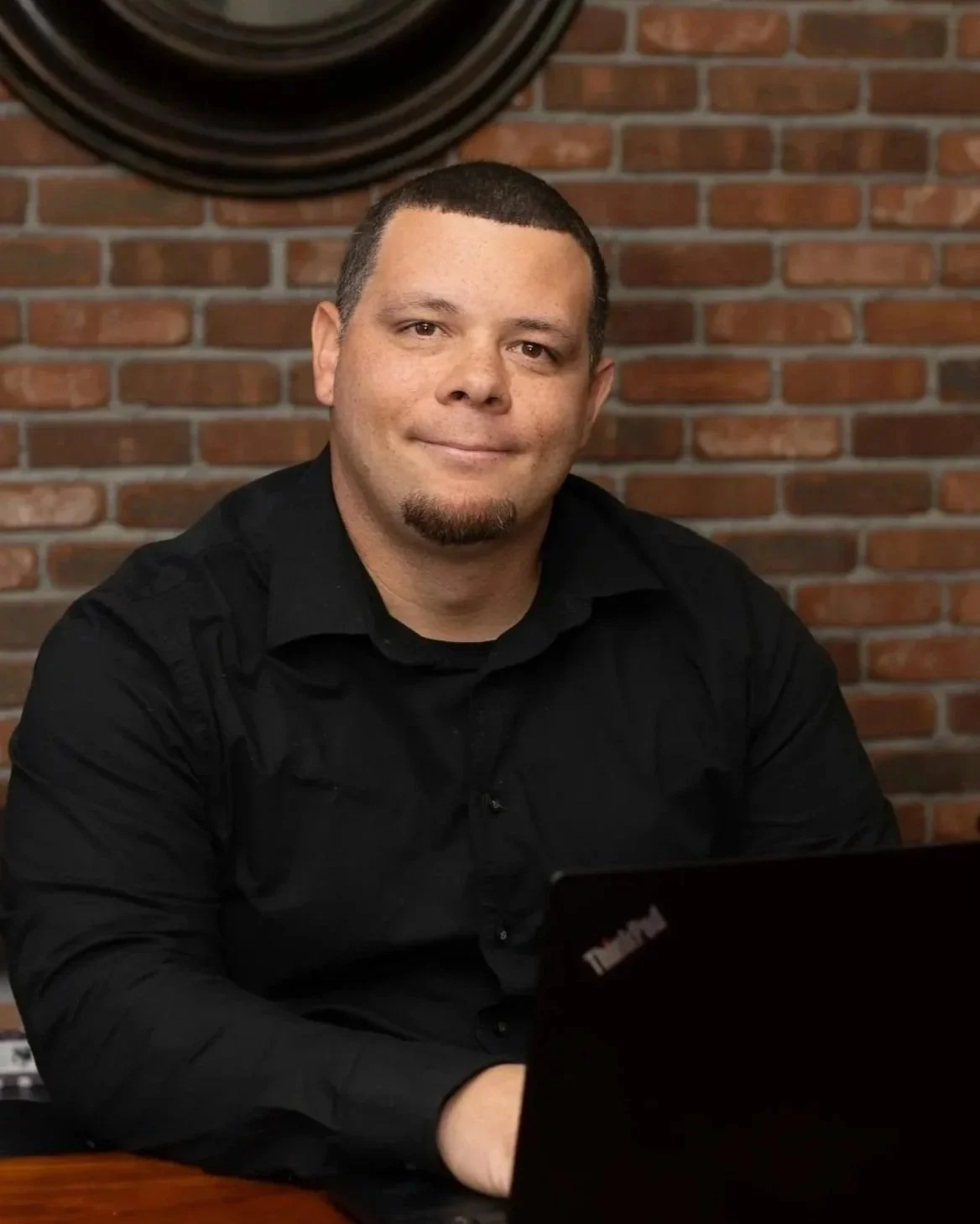 Nate Alvarez sitting at a desk in front of a brick wall