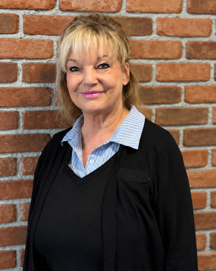 Lori Marsh is standing against a red brick wall, smiling at the camera.