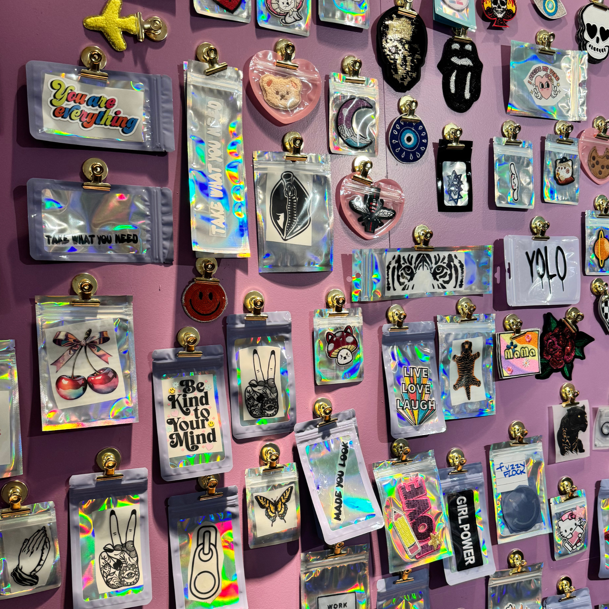 Colorful patches and pins with various designs on a pink wall, including text, cartoon characters, and symbols.
