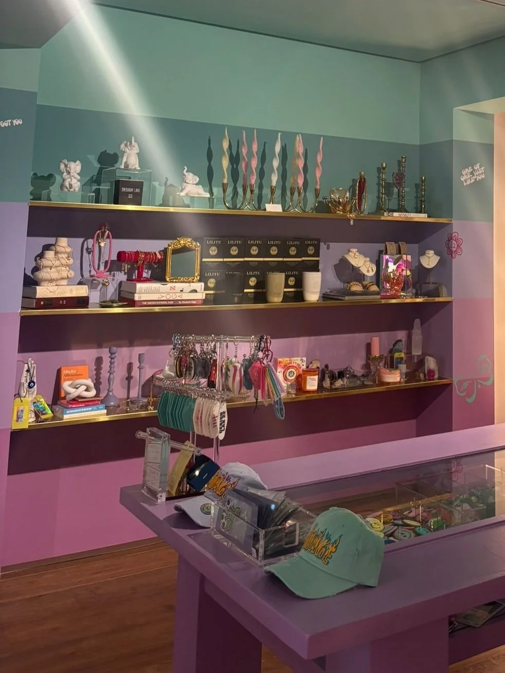 Colorful retail display with shelves holding various accessories, jewelry, and decorative items, against pastel-colored walls.