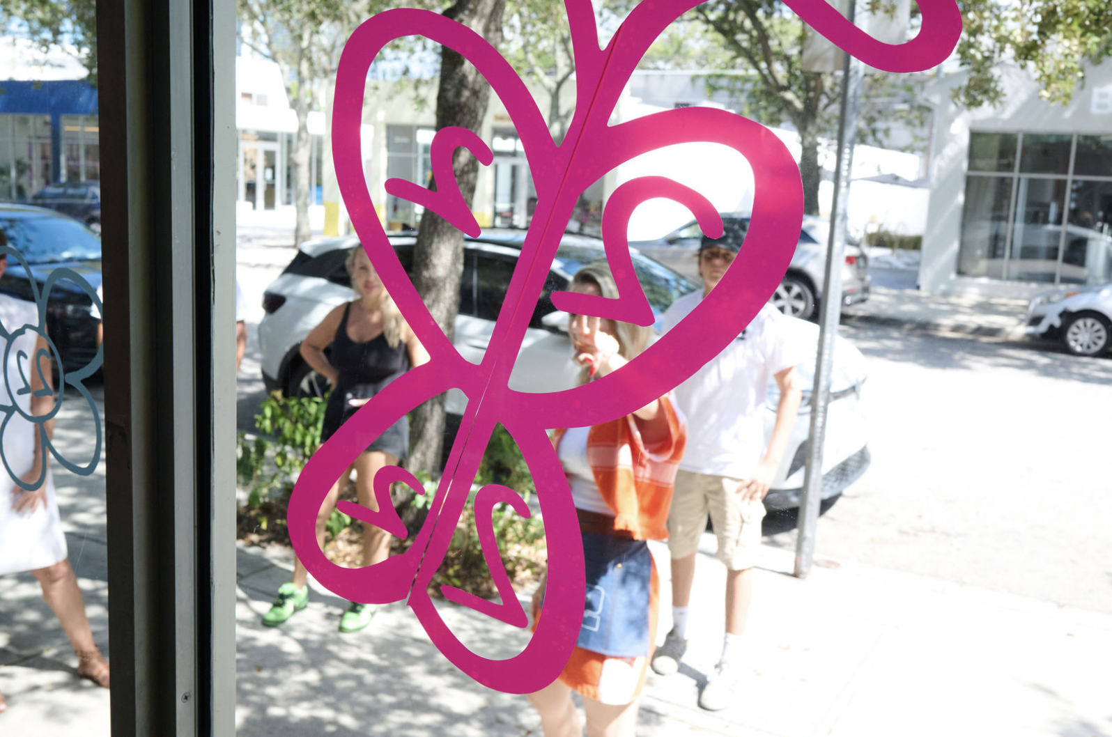 People standing outside viewed through a glass window with pink butterfly design.