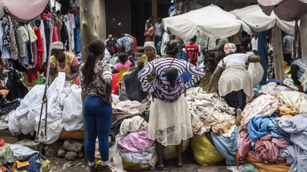 Market scene with women and children shopping for clothes and textiles.