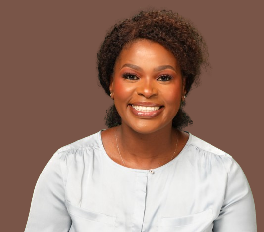 Portrait of a smiling African American woman with curly hair wearing a white top, against a brown background.