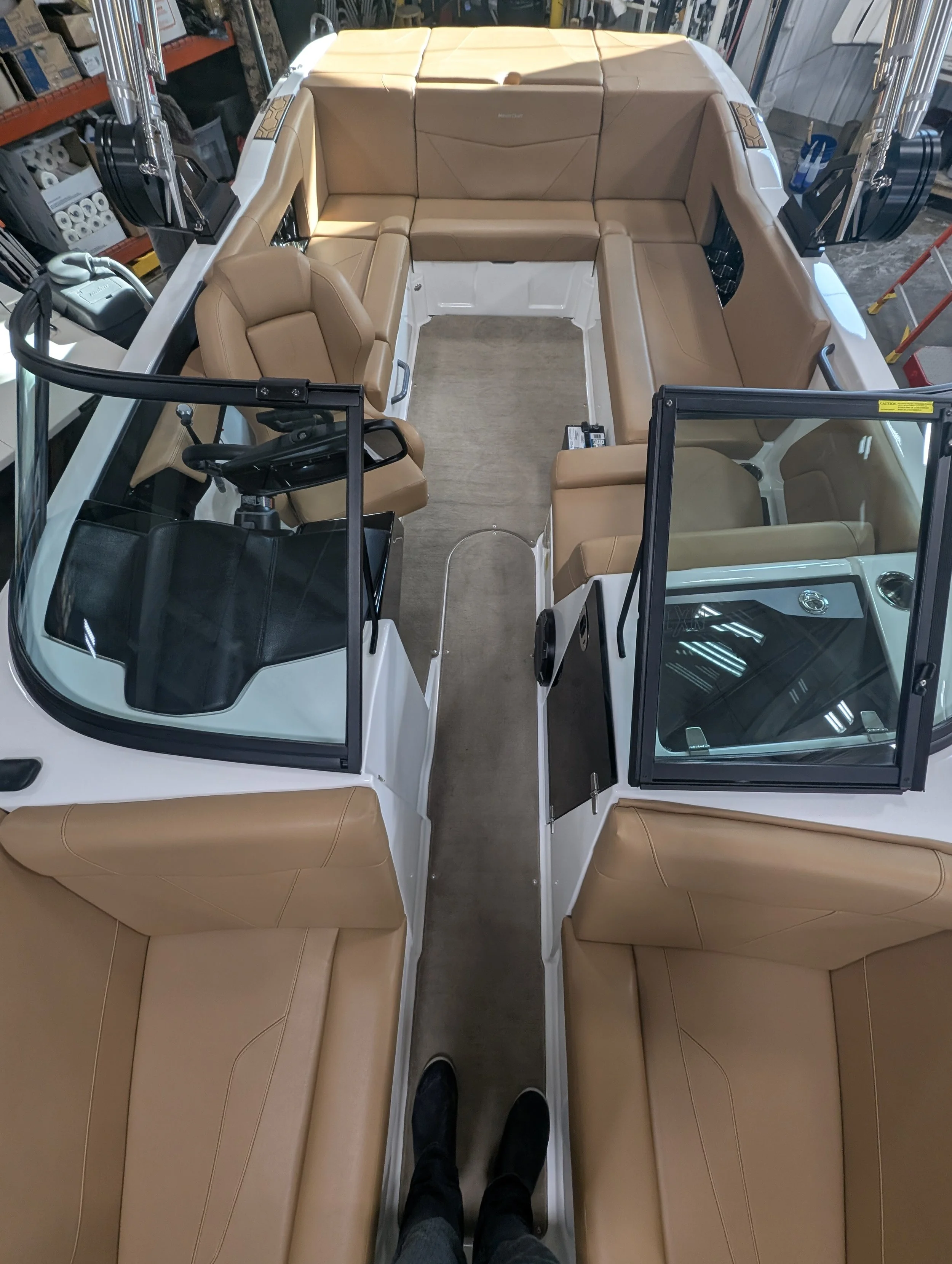 Inside view of a white boat with tan leather seats arranged in a U-formation around the edges and a walkway in the middle, taken from the perspective of someone standing on the walkway.