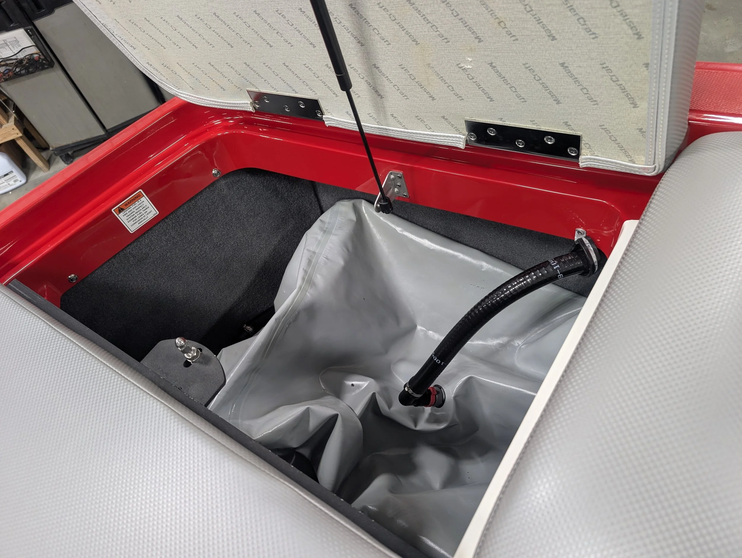 Empty storage compartment in a vintage vehicle with a red interior, a black hose, and fabric lining.