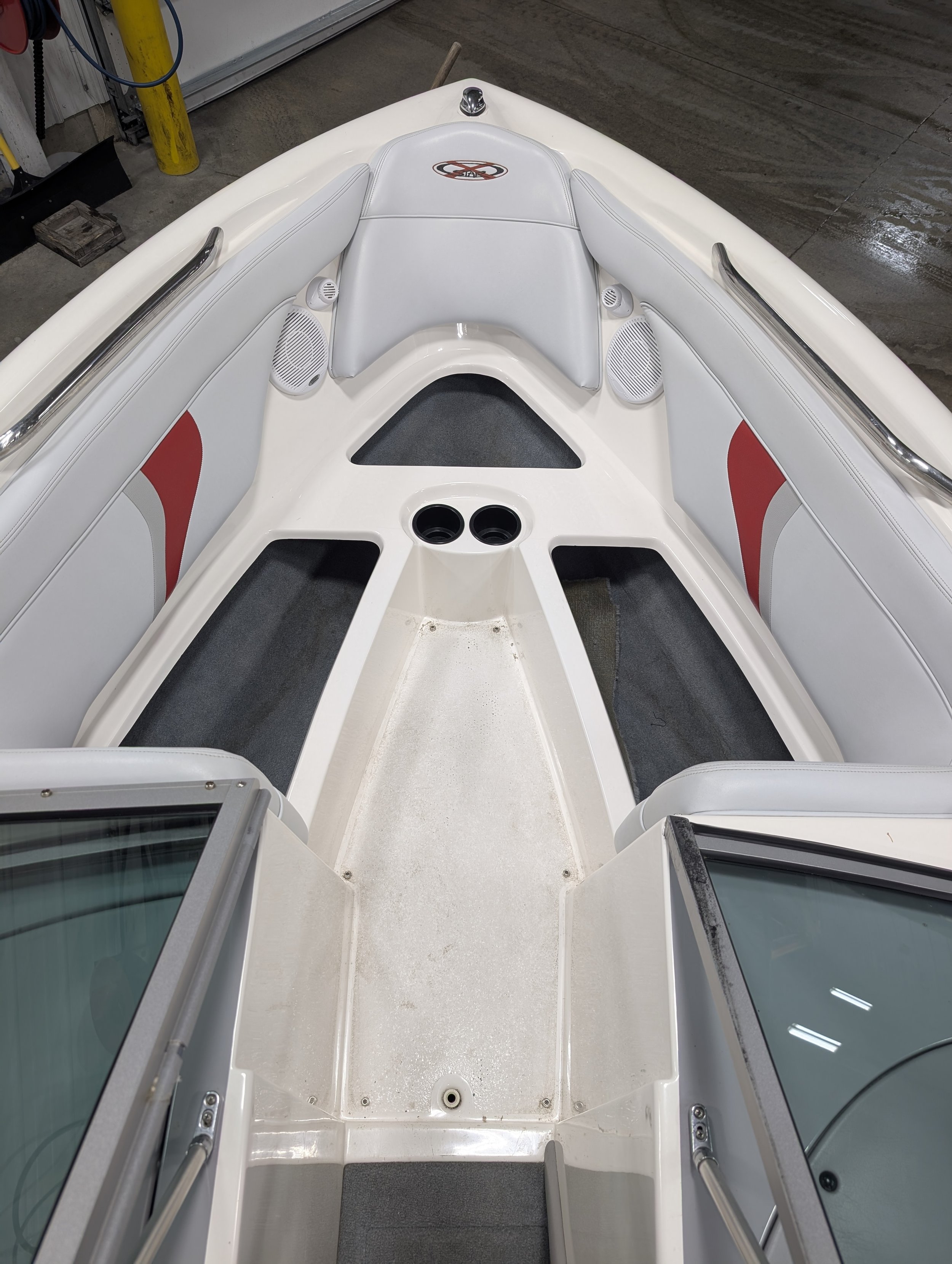 The interior front section of a white speedboat with seating, speakers, cup holders, and a windshield.
