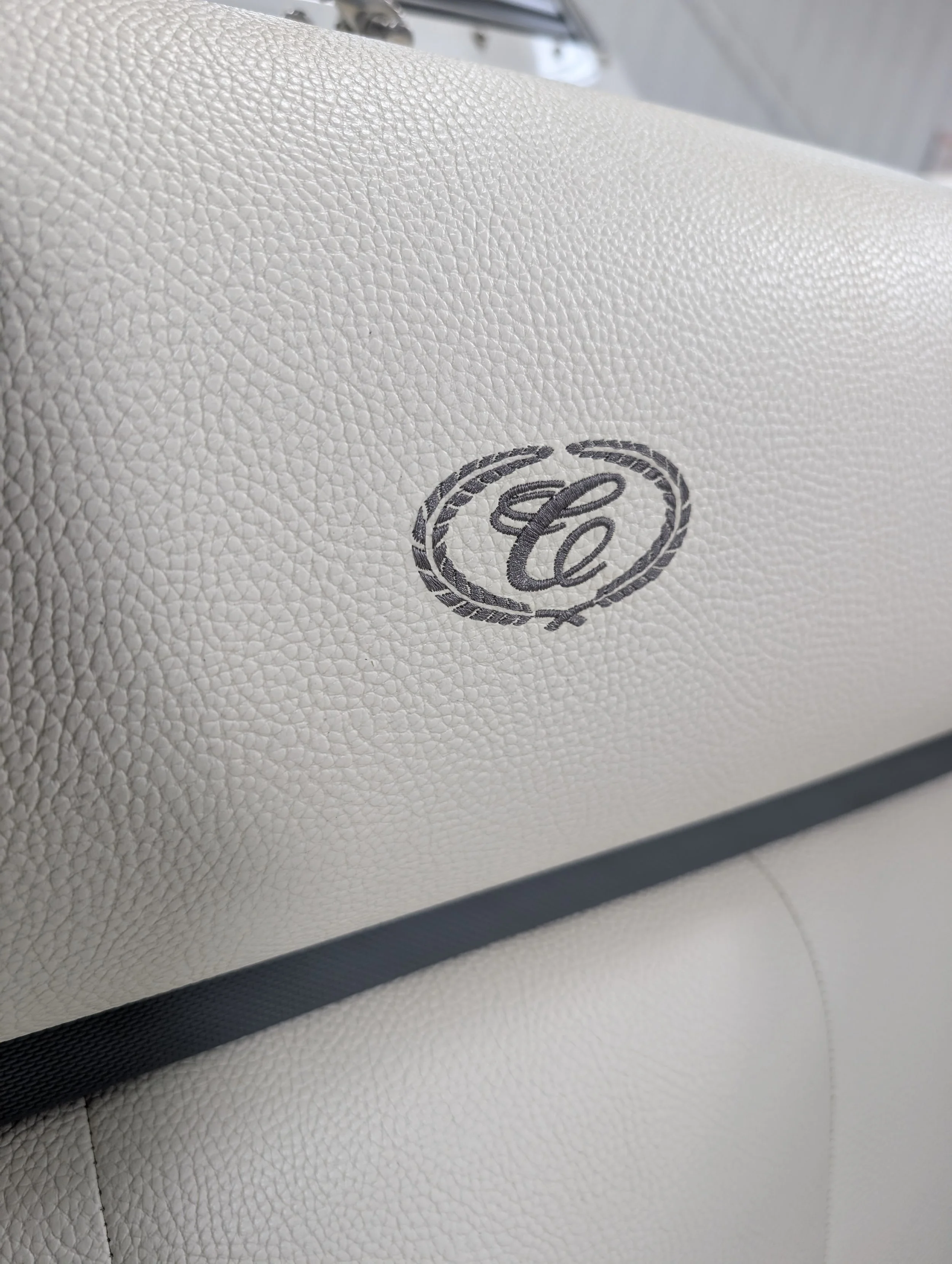 Close-up of a beige leather surface with a logo featuring an intertwined 'C' inside a circular design.