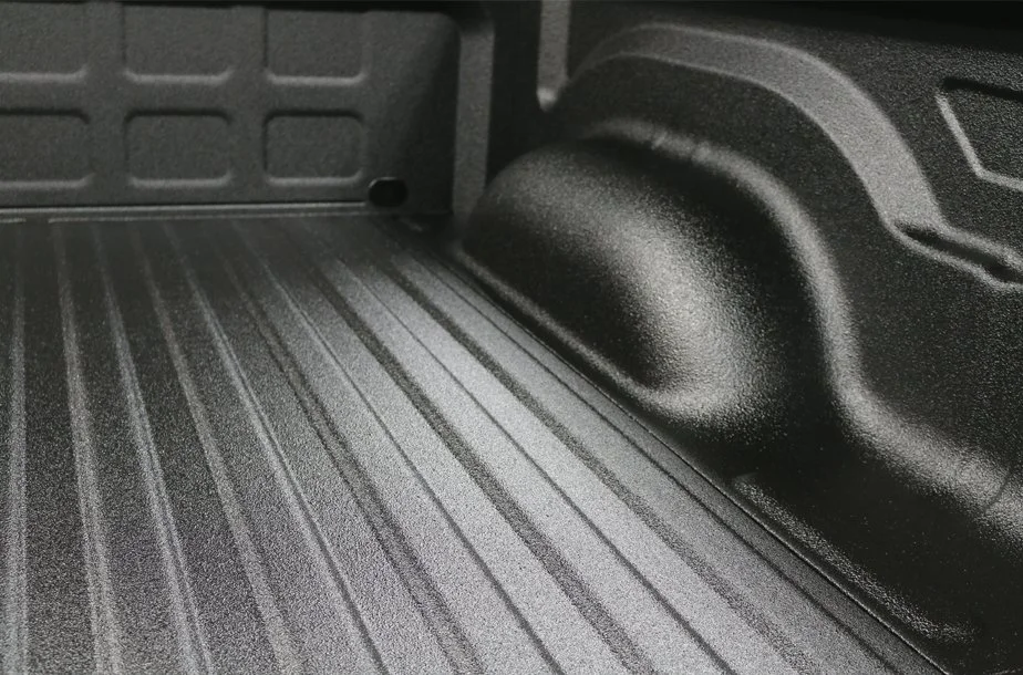 Close-up of a truck bed with textured black surface and wheel well.
