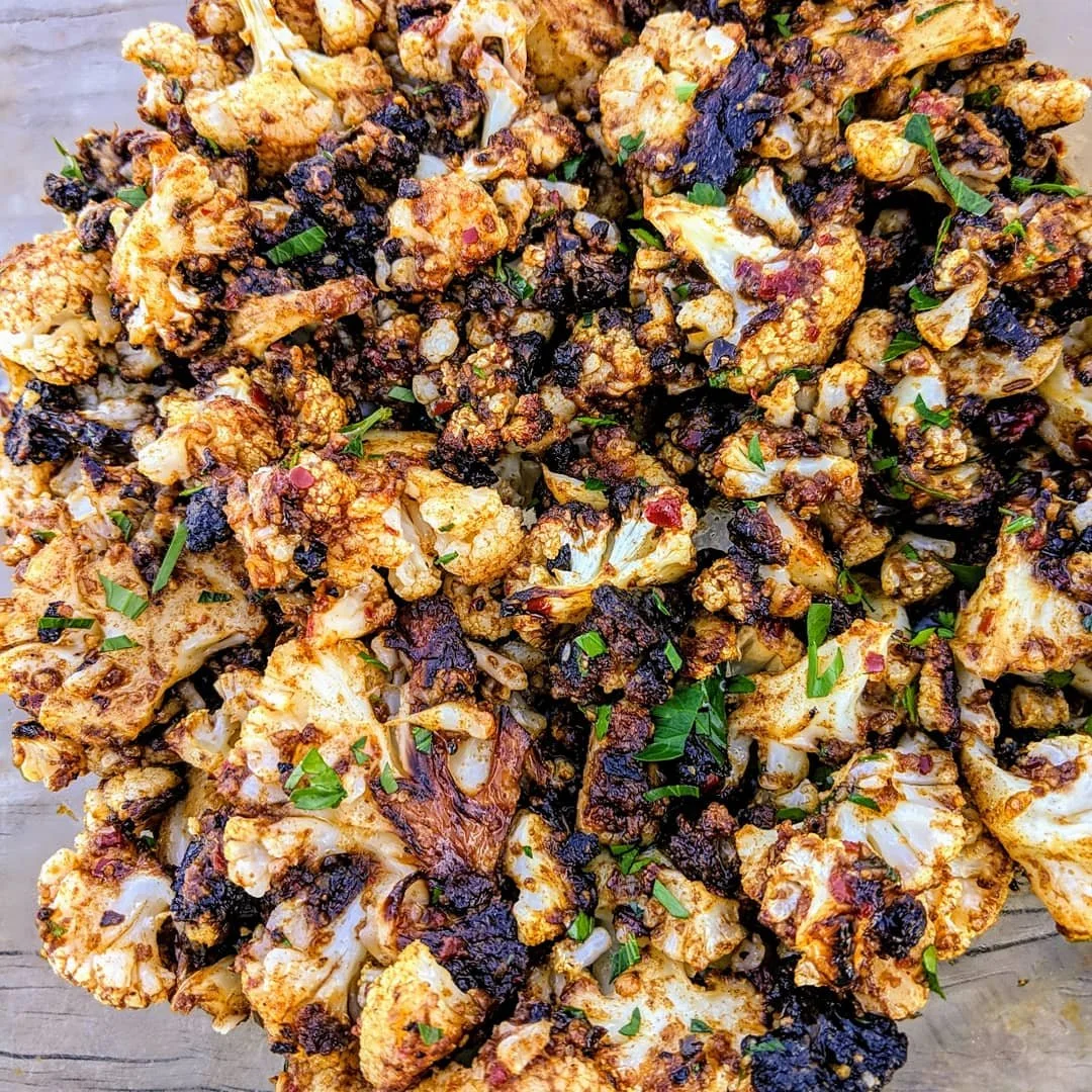 Roasted or grilled cauliflower florets topped with a spice mixture, garnished with chopped parsley.