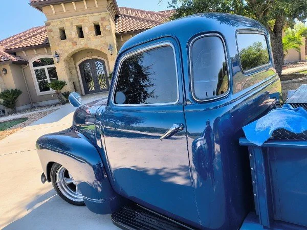 A vintage blue pickup truck parked in front of a house with a gated entrance and stone facade.