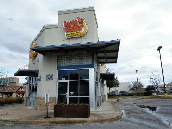 Exterior of a Burger King fast food restaurant with a sign reading 'family burger' and an image of a banana, on a cloudy day with a wet parking lot.
