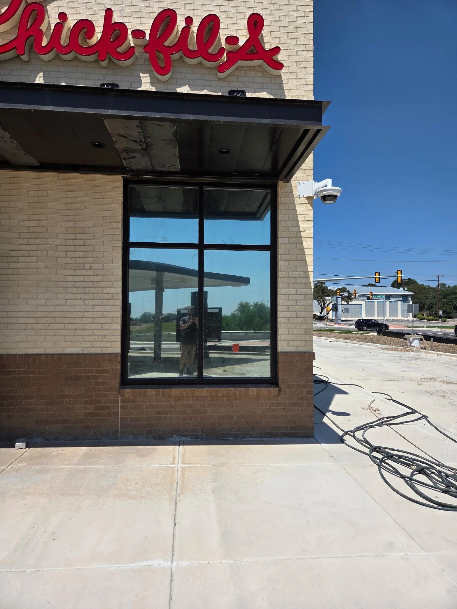 Exterior view of a Chick-fil-A restaurant under construction with a large window, security camera, and the Chick-fil-A sign on the wall.