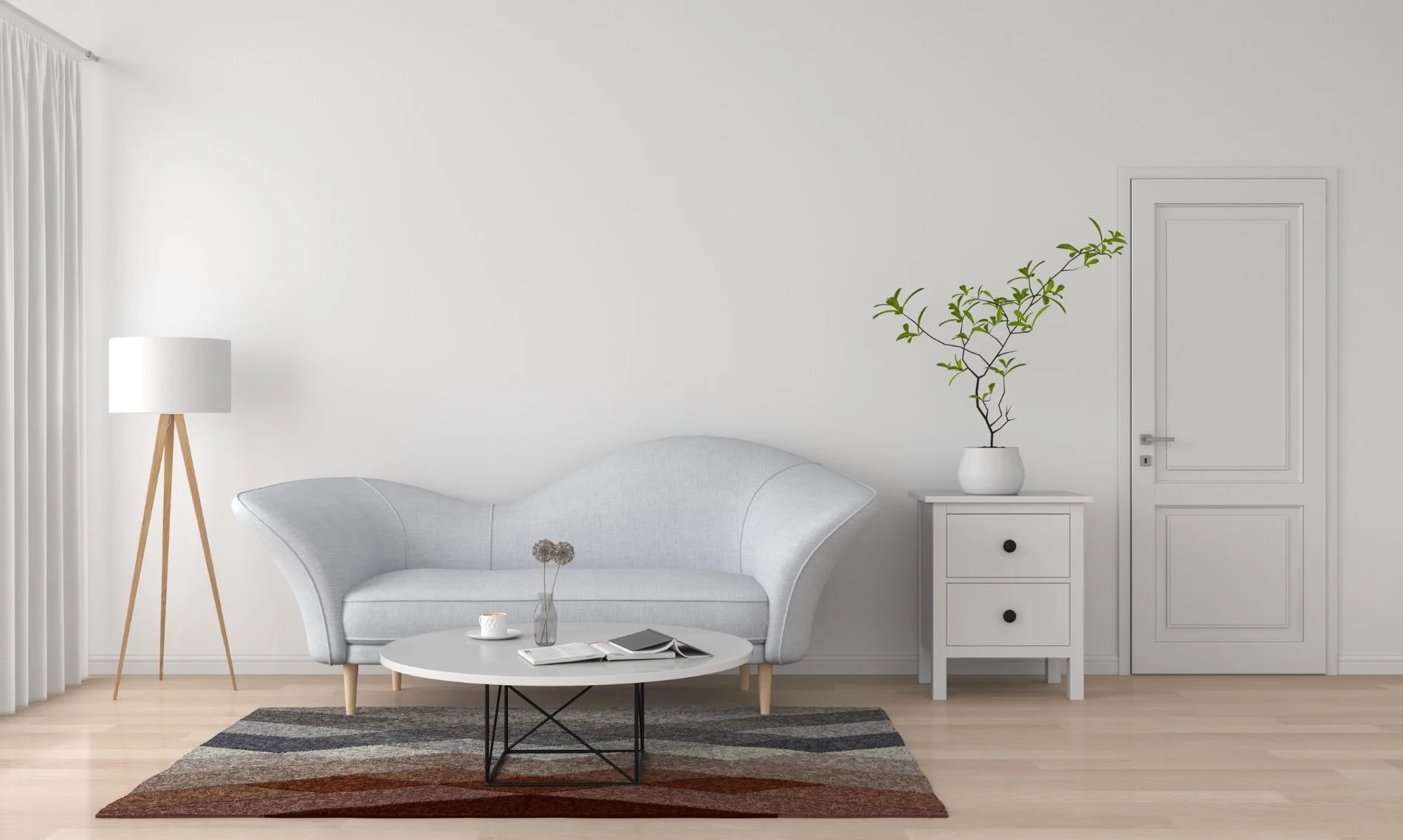 Minimalist living room with a white curved sofa, a white side table with drawer, a white vase with green branches, a tall wooden floor lamp, and a multicolored area rug on light wooden floor, against white walls with a door.