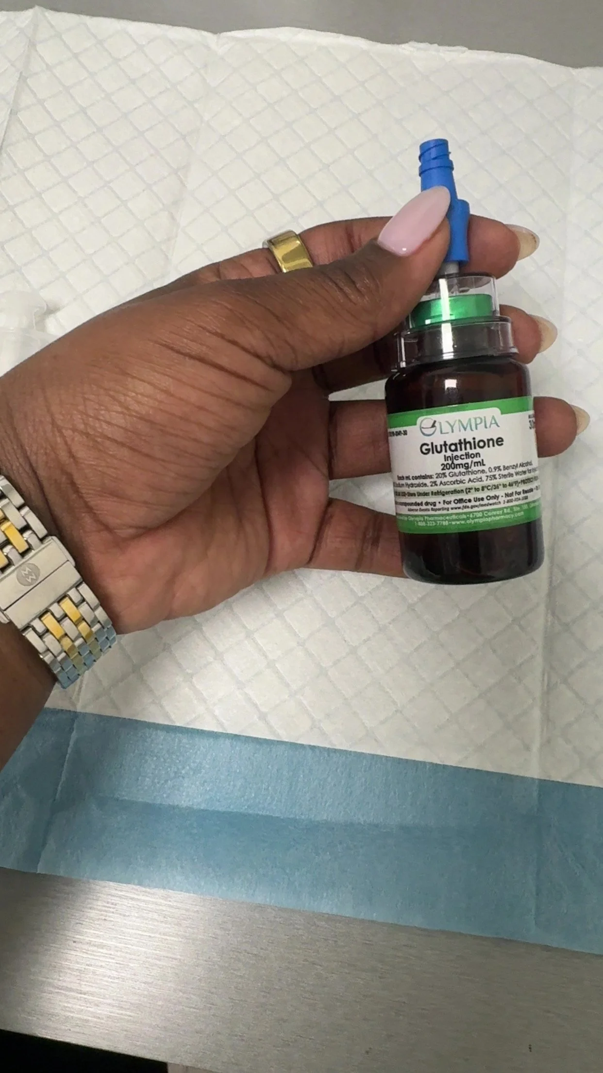 Close-up of a hand holding a vial labeled Glutathione, with a syringe inserted into the vial, on a medical tray with a white sheet.
