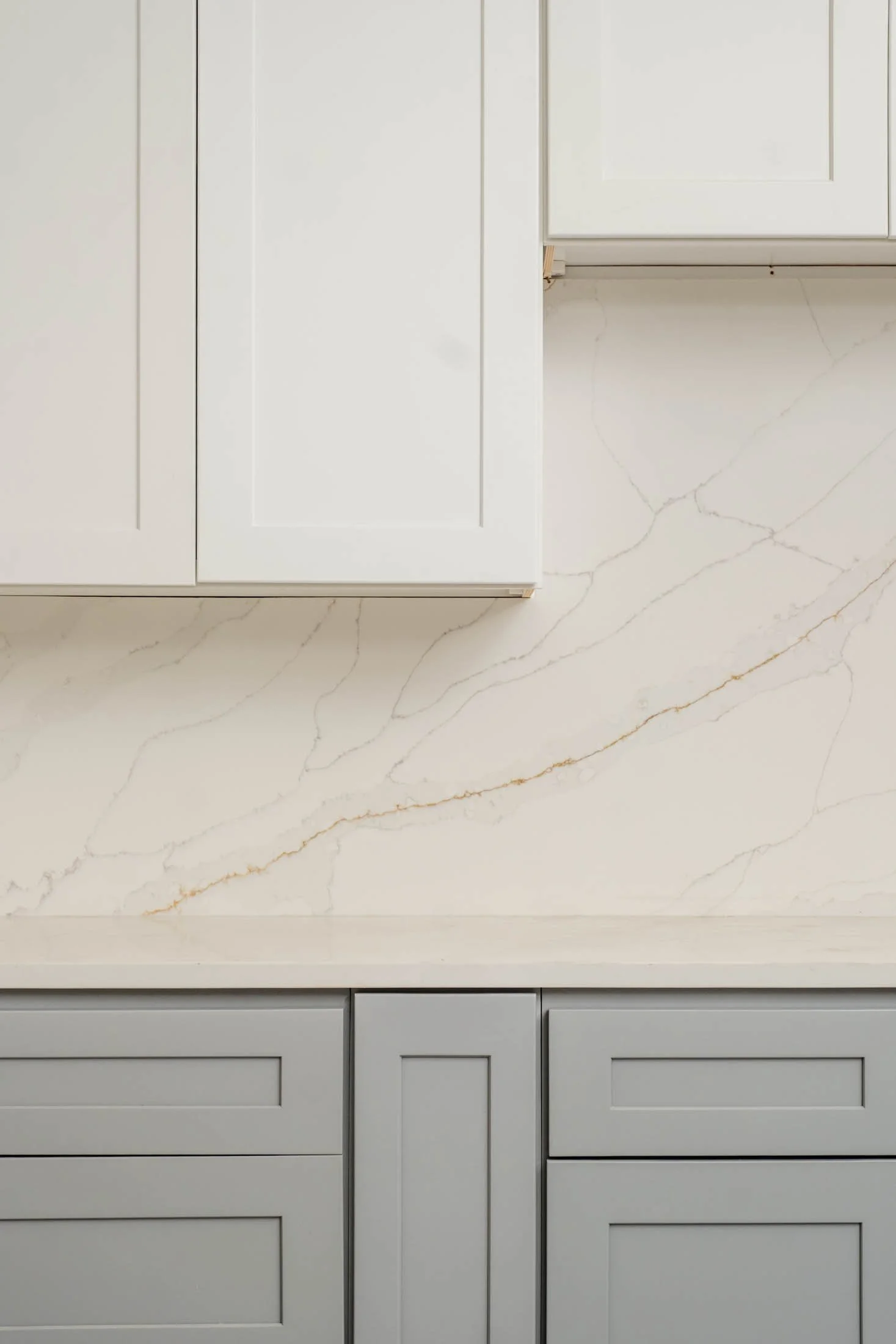 Close-up of a marble kitchen countertop with white and gold veining, and upper and lower cabinets in light gray and white.
