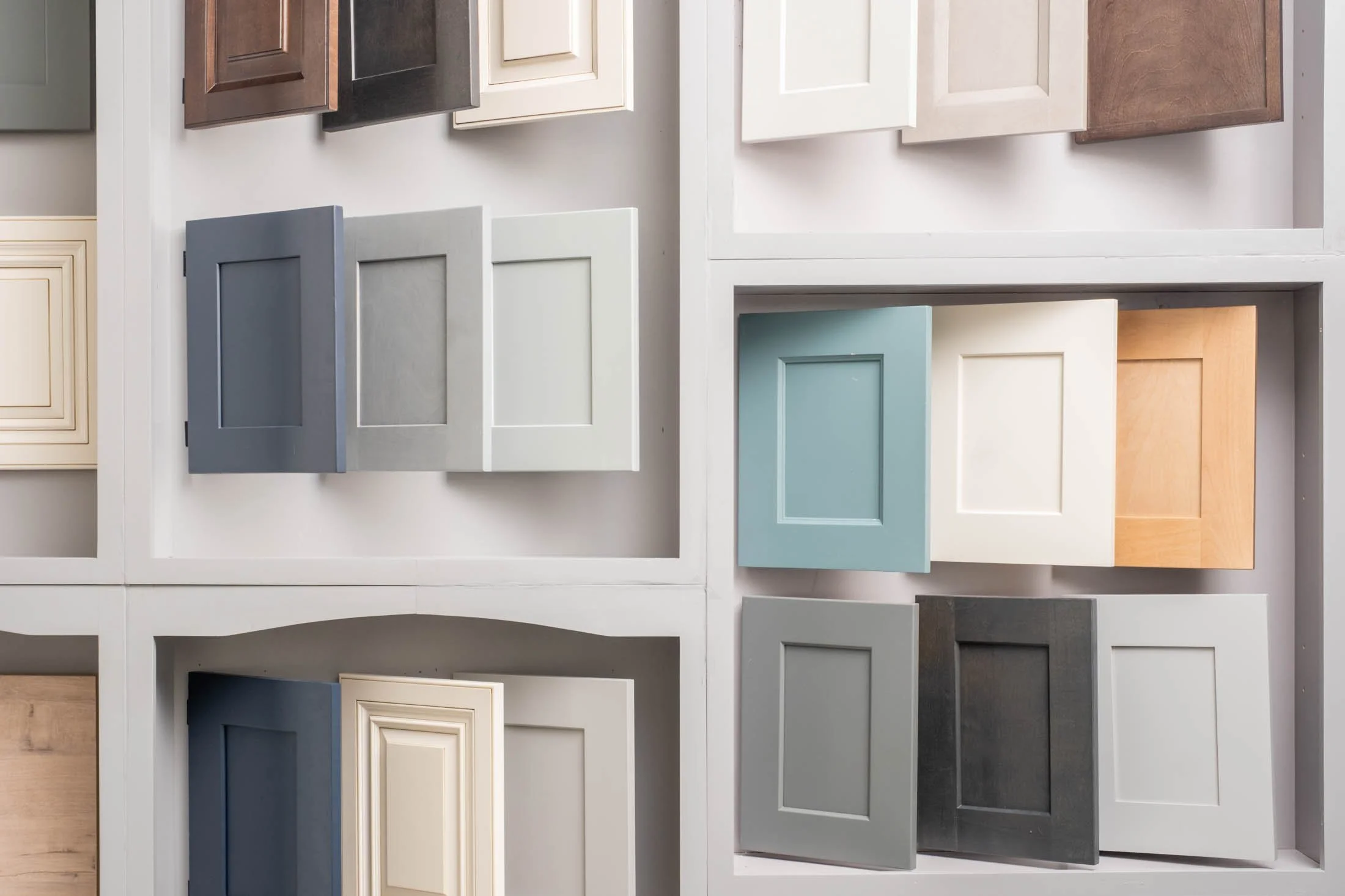 Display of various cabinet doors in different colors and finishes arranged on a wall.