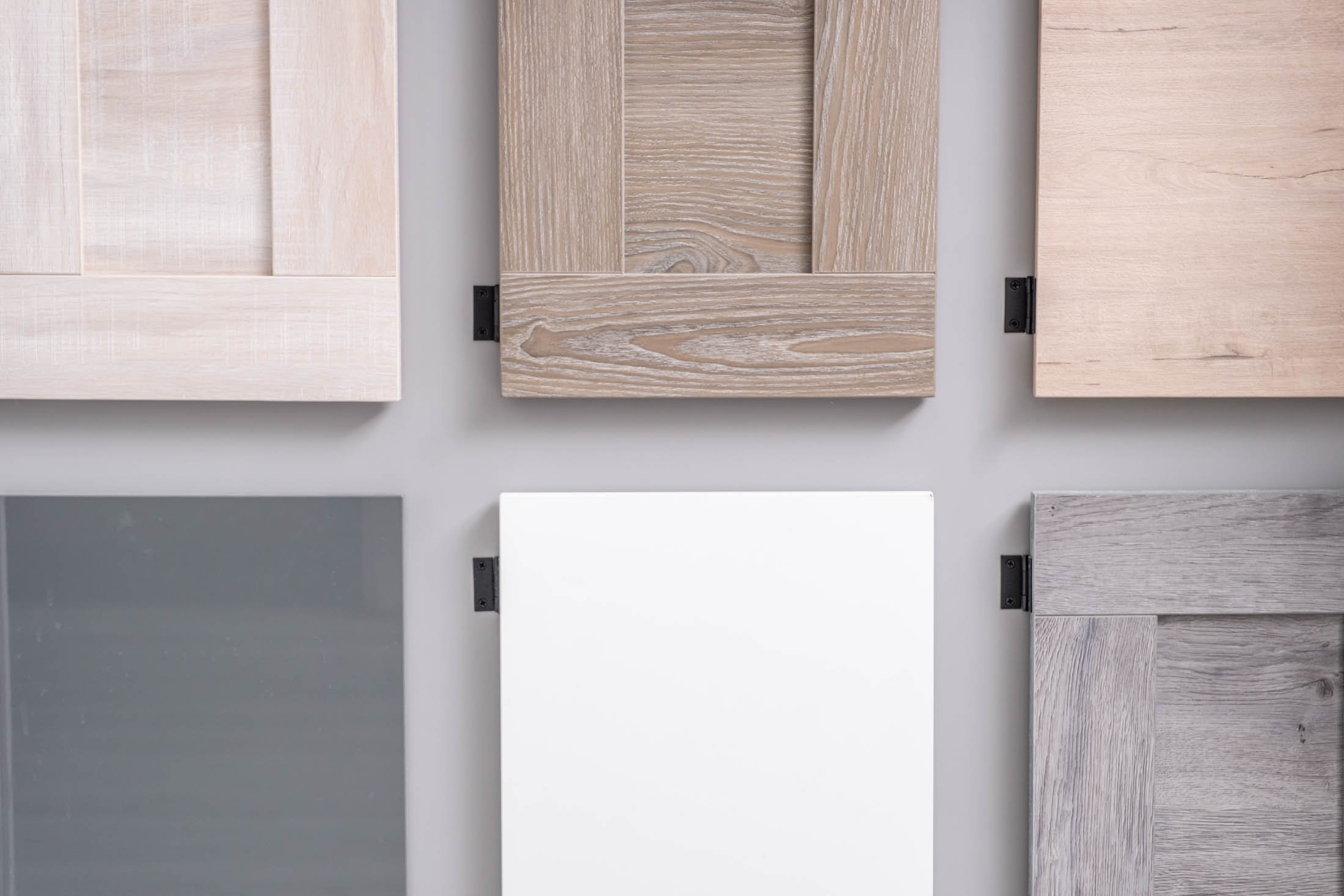 A collection of six photo samples of wood and metal panels, each with a different finish, arranged on a wall.