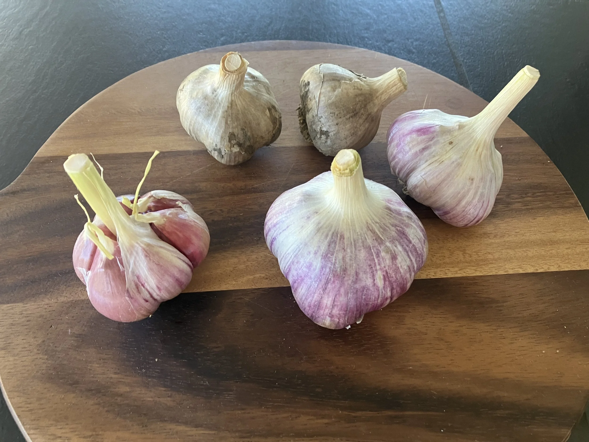 Several bulbs of garlic, some with papery outer layers, are placed on a two-tone wooden cutting board.