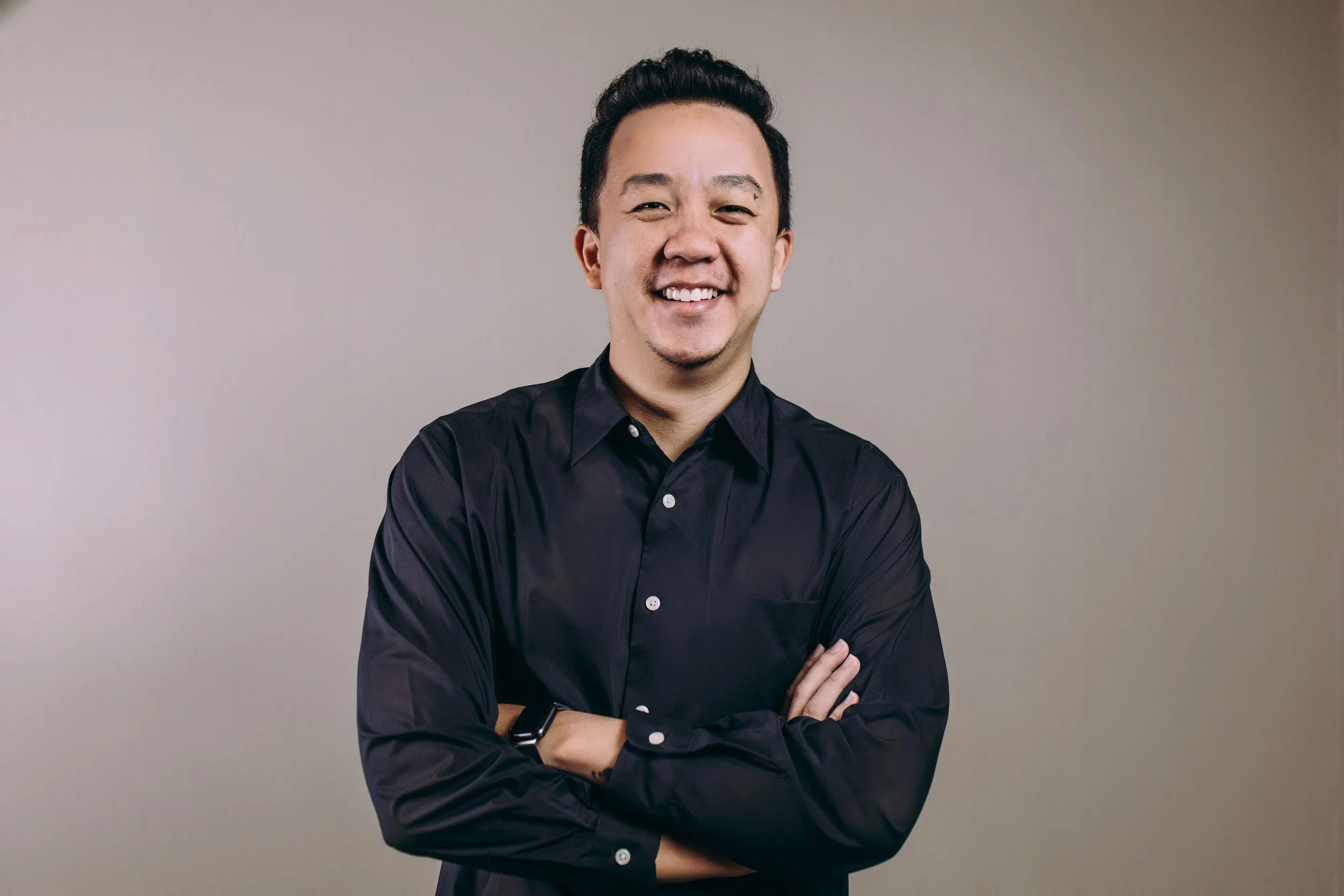 Smiling man in a black suit and blue shirt against a gray background.