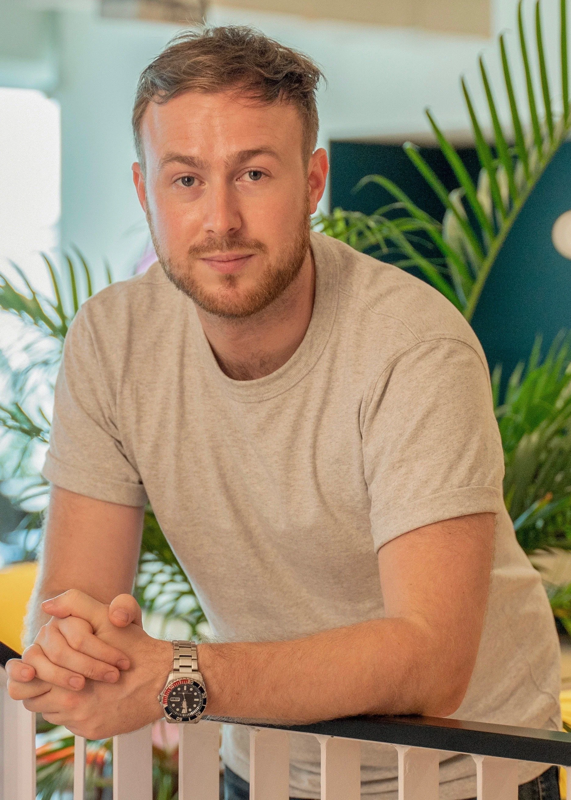 Man in a white shirt stands on a balcony with city skyscrapers in the background.
