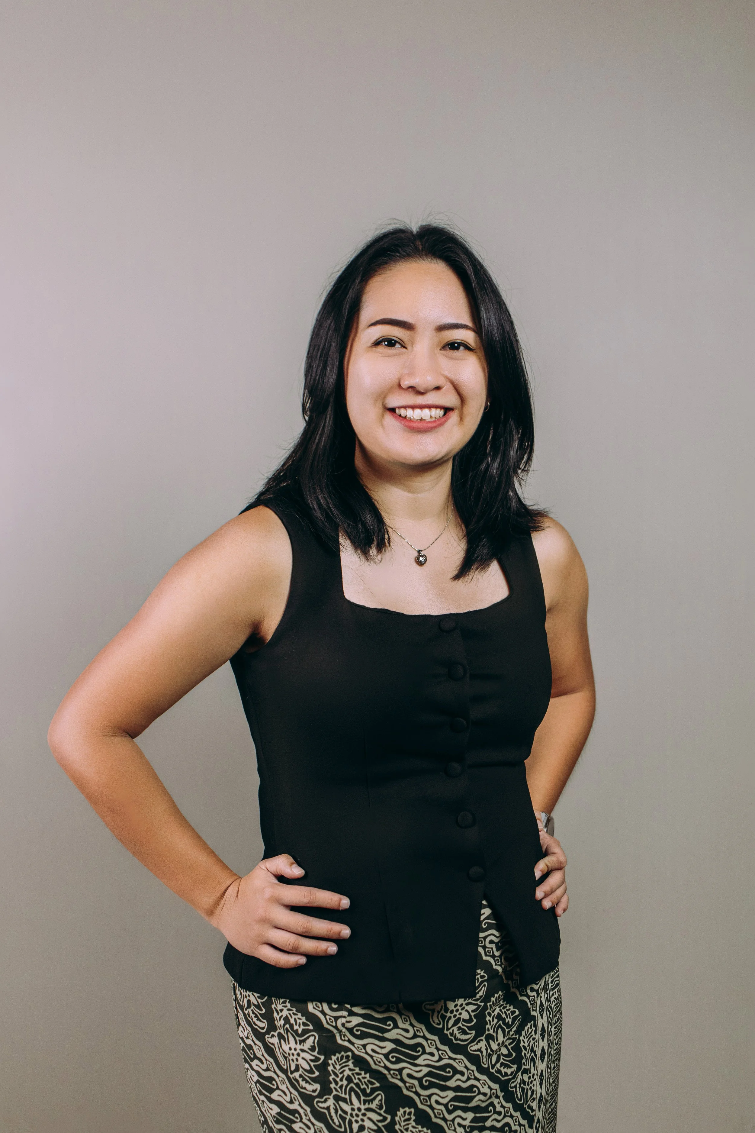 Smiling person in a white shirt standing on a balcony with city buildings in the background.