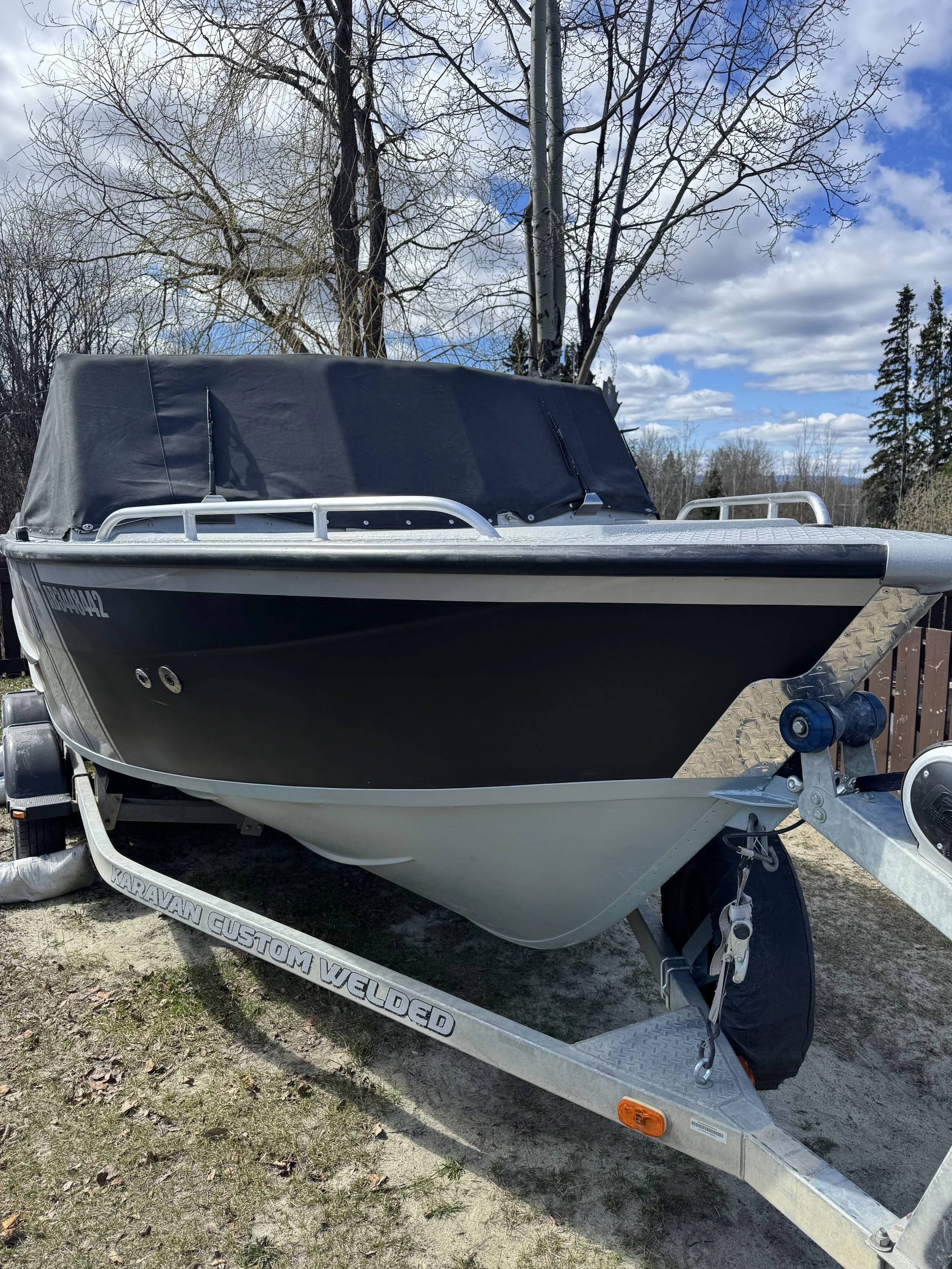 A small black and white boat on a trailer, parked outdoors, with a tree and partly cloudy sky in the background.