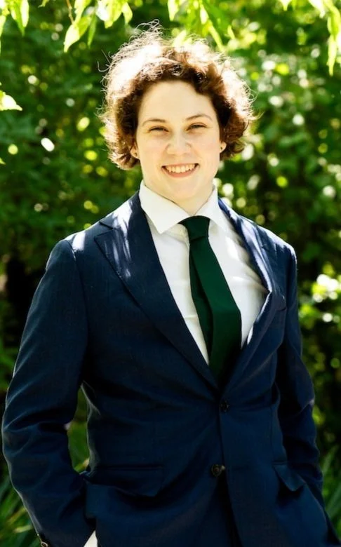 Person in a blue suit and green tie smiling outdoors