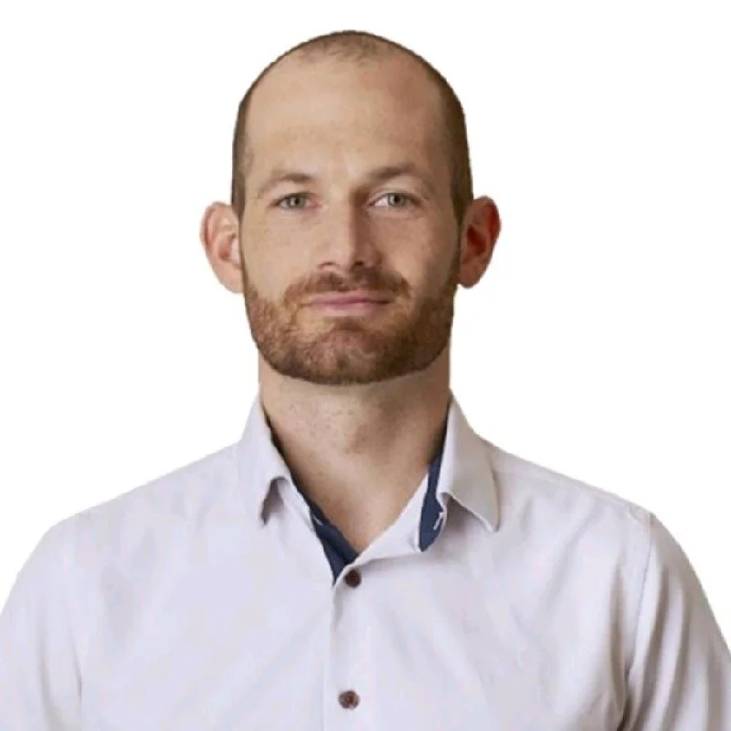 Man in a white shirt with a beard standing against a plain white background.
