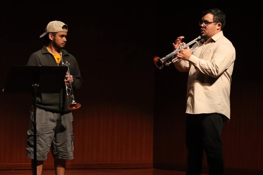 Two men playing trumpets on a stage with a dark background.