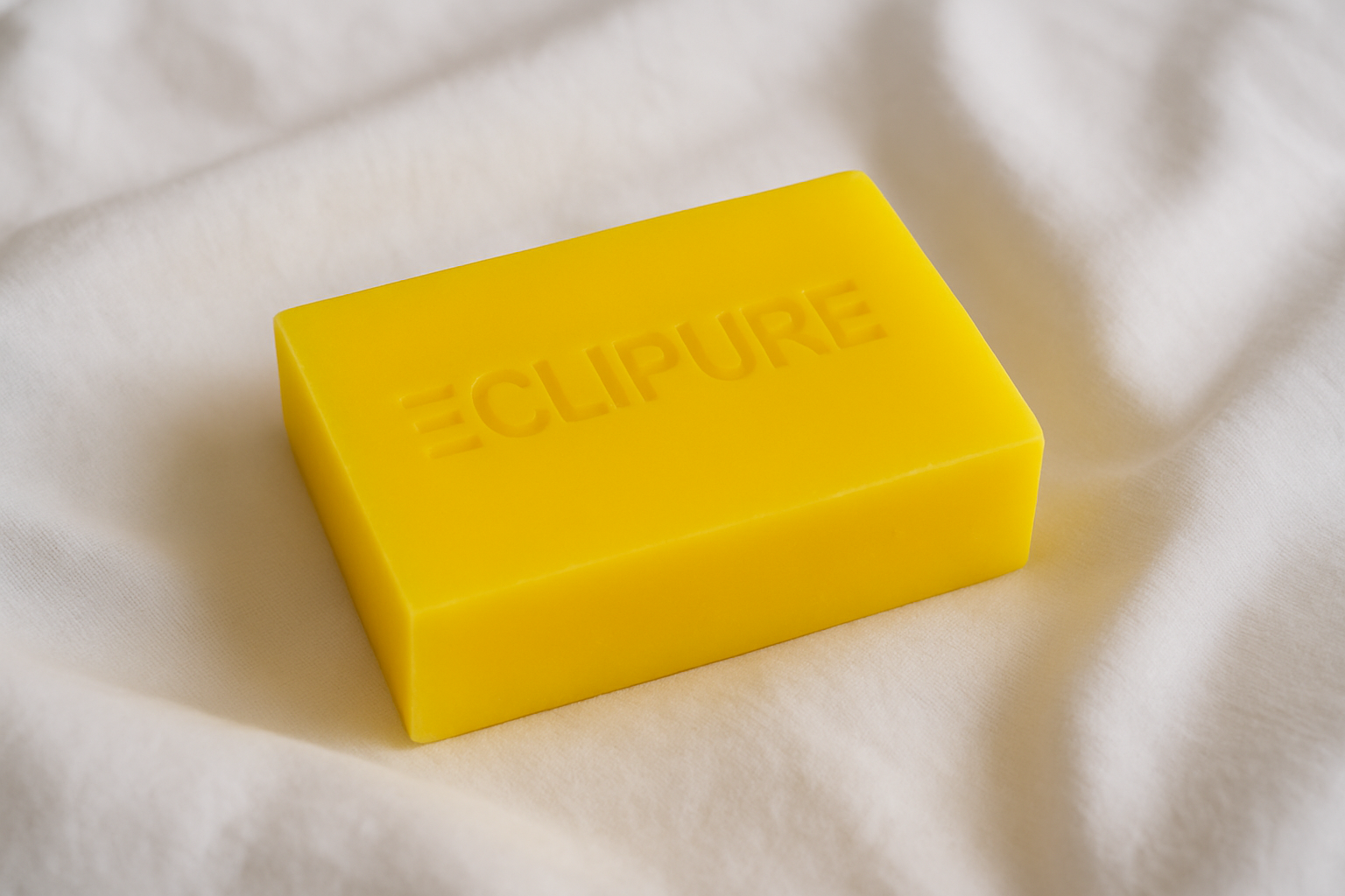 A yellow bar of soap with the word 'CUPURE' embossed on it, resting on white fabric.