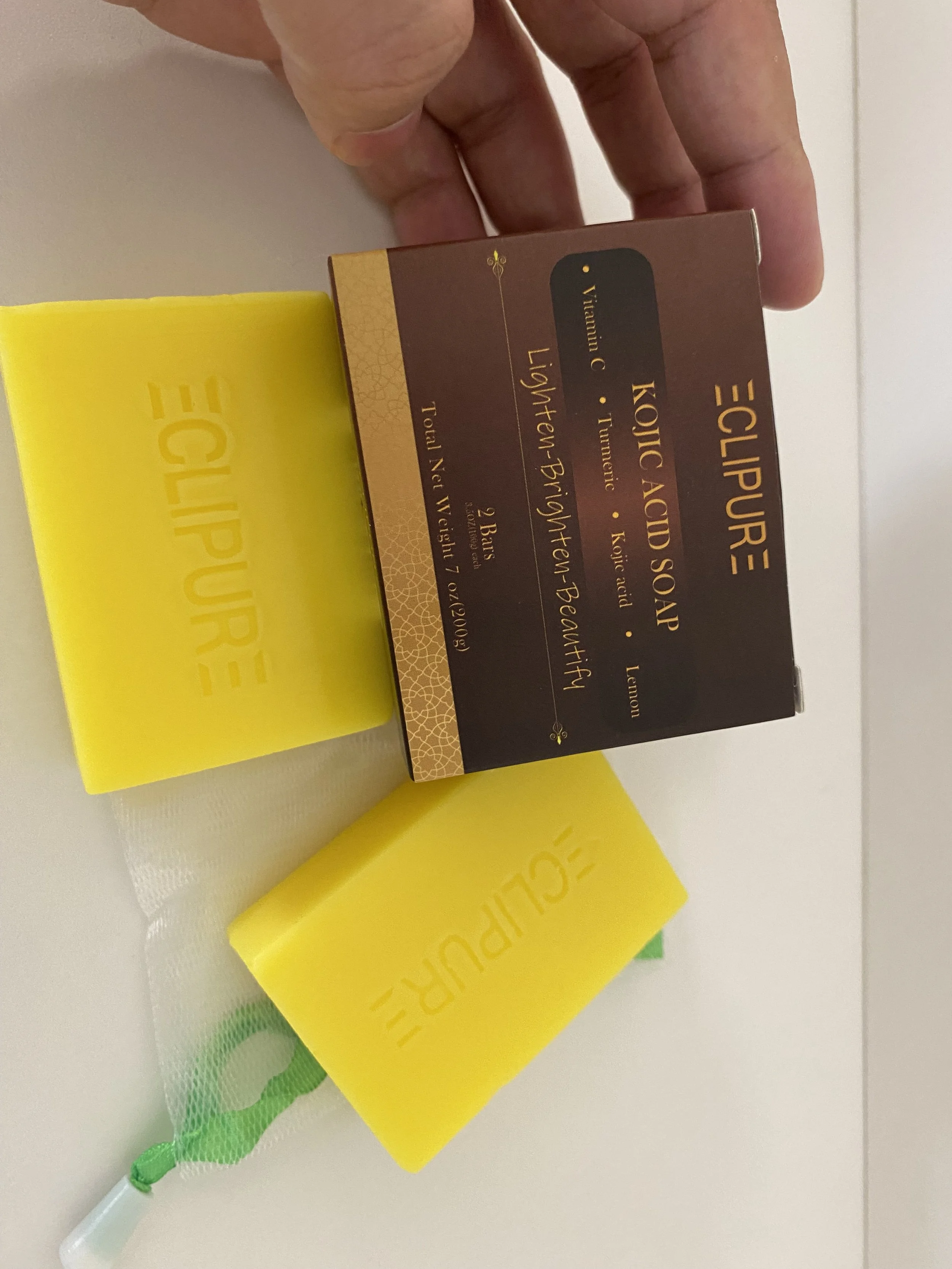 Box of Kojic Acid Soap with a yellow soap bar beside it, on a white surface. The soap bar has embossed text that reads 'ECLIPURE'.