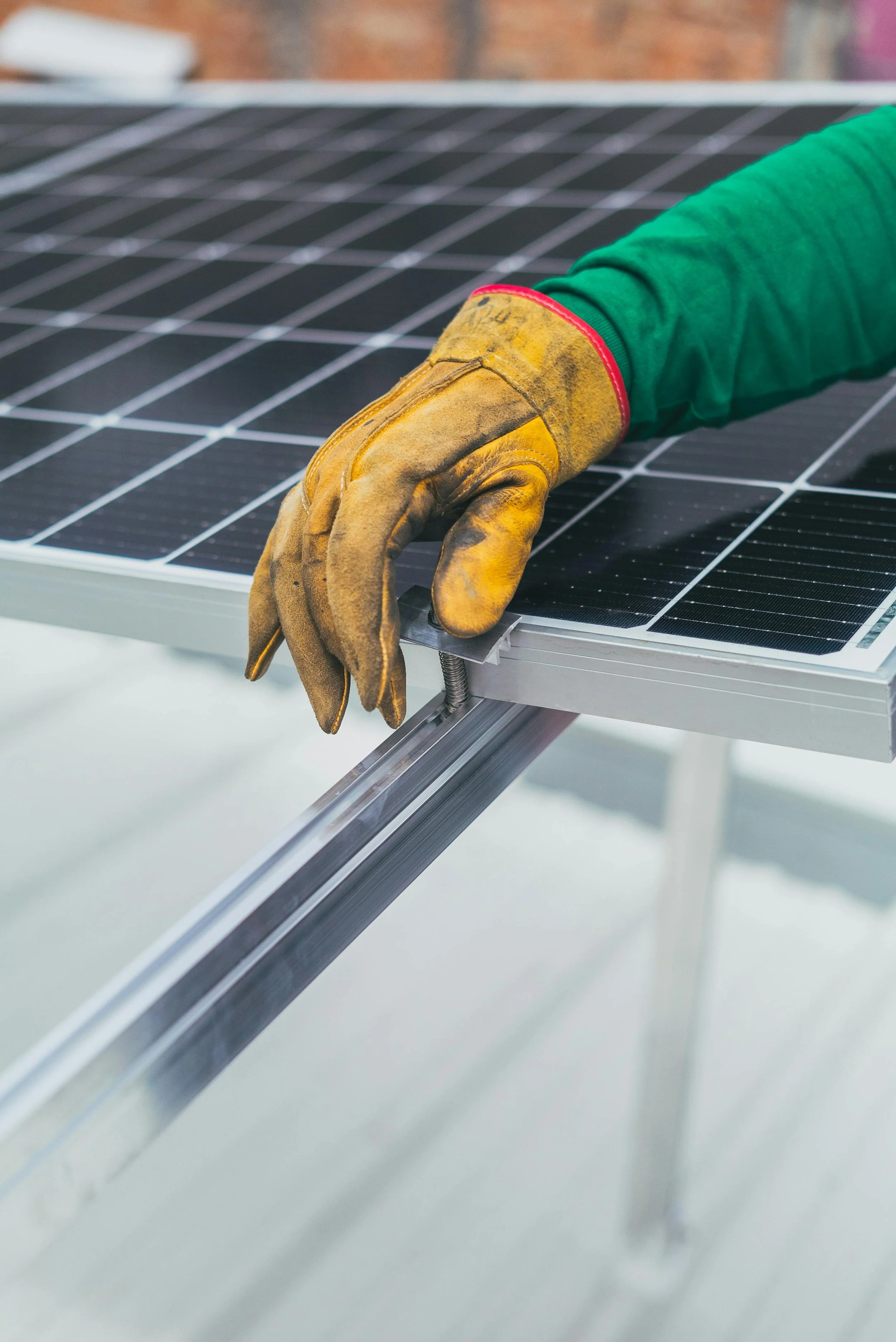 Una mano con guante de trabajo ajusta un panel solar en un marco metálico.
