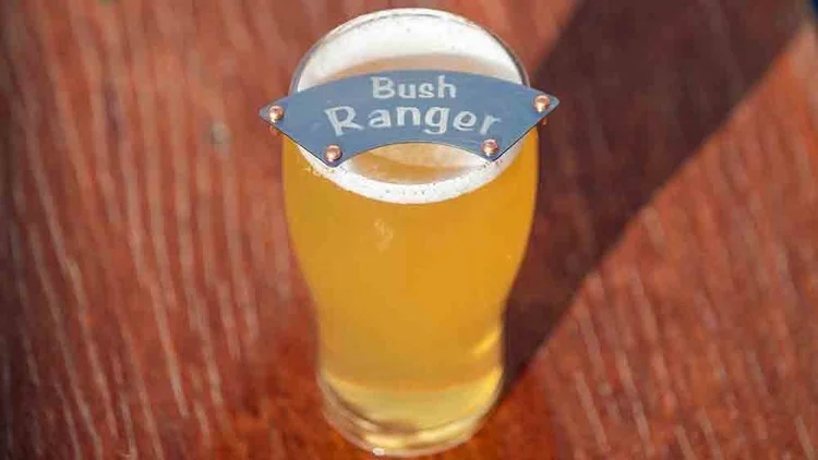 Glass of light-coloured beer with a "Bush Ranger" moustache protector on top.