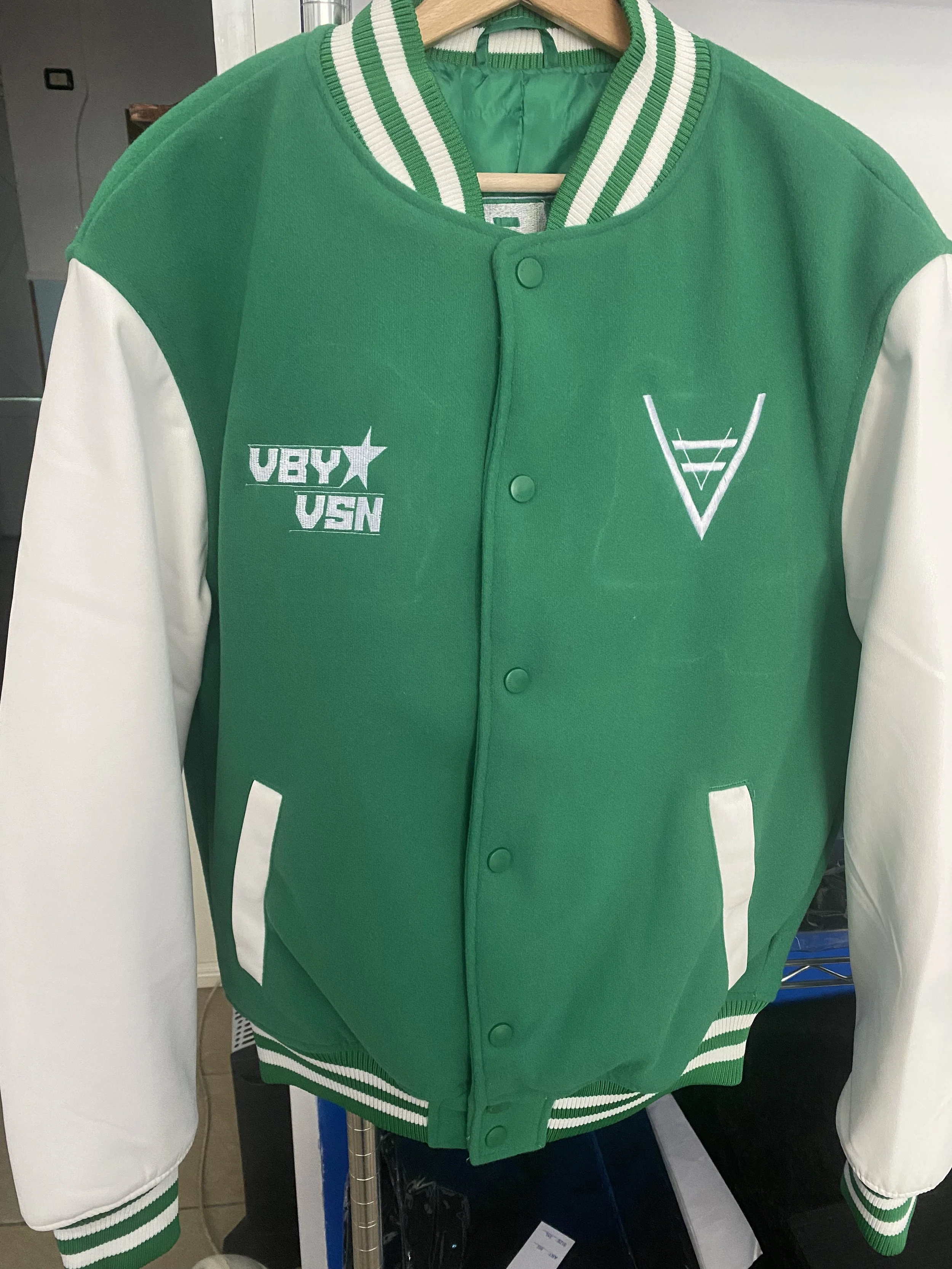 Giacca sportiva verde con maniche bianche, collo a righe verdi e bianche, e tasche bianche. Sono presenti loghi e scritte sulla parte anteriore.