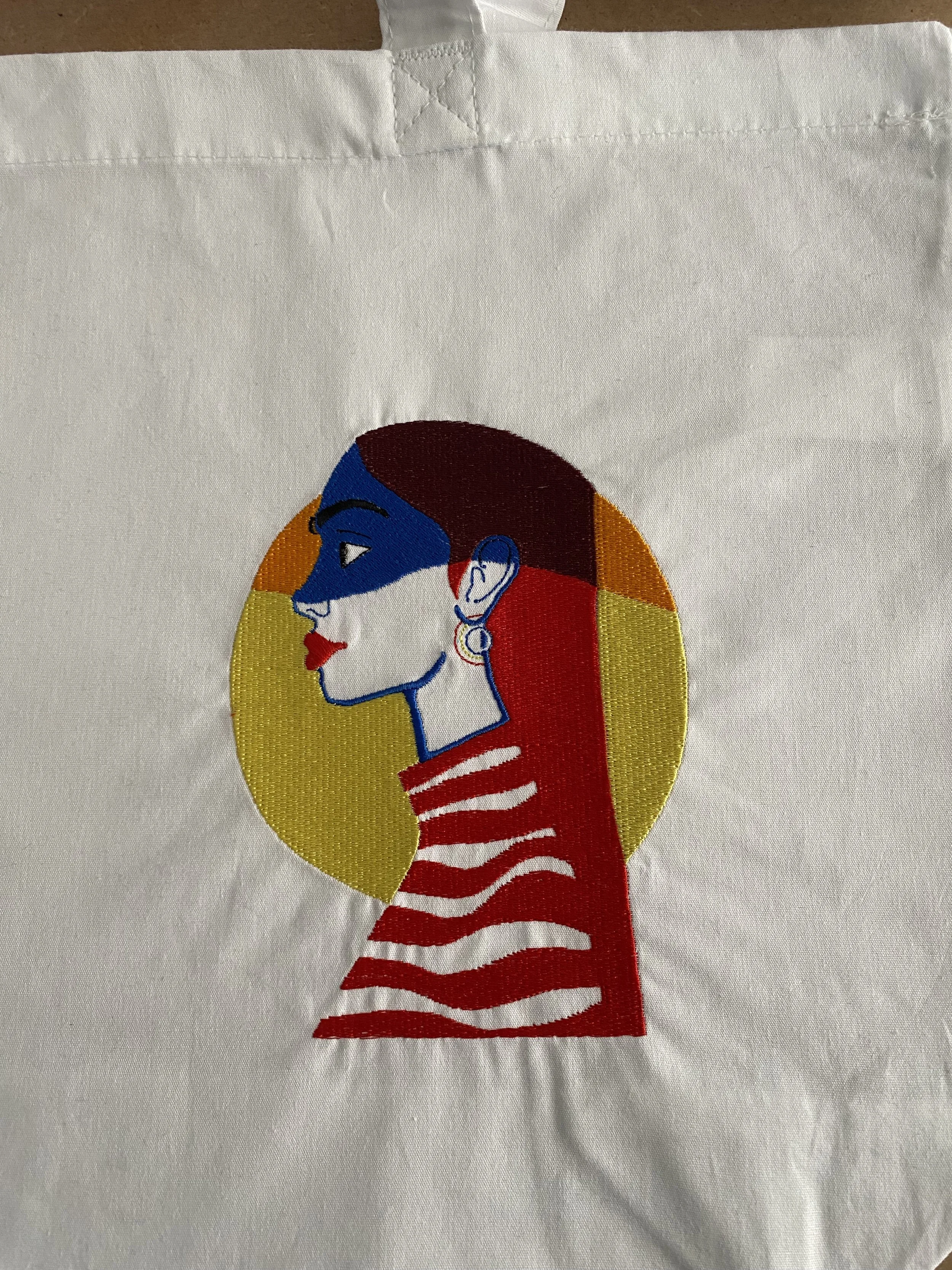 Disegno di un profilo di donna con colori vivaci, sfondo circolare giallo, capelli rossi, trucco colorato e orecchino, con una maglietta a righe rosse e bianche.