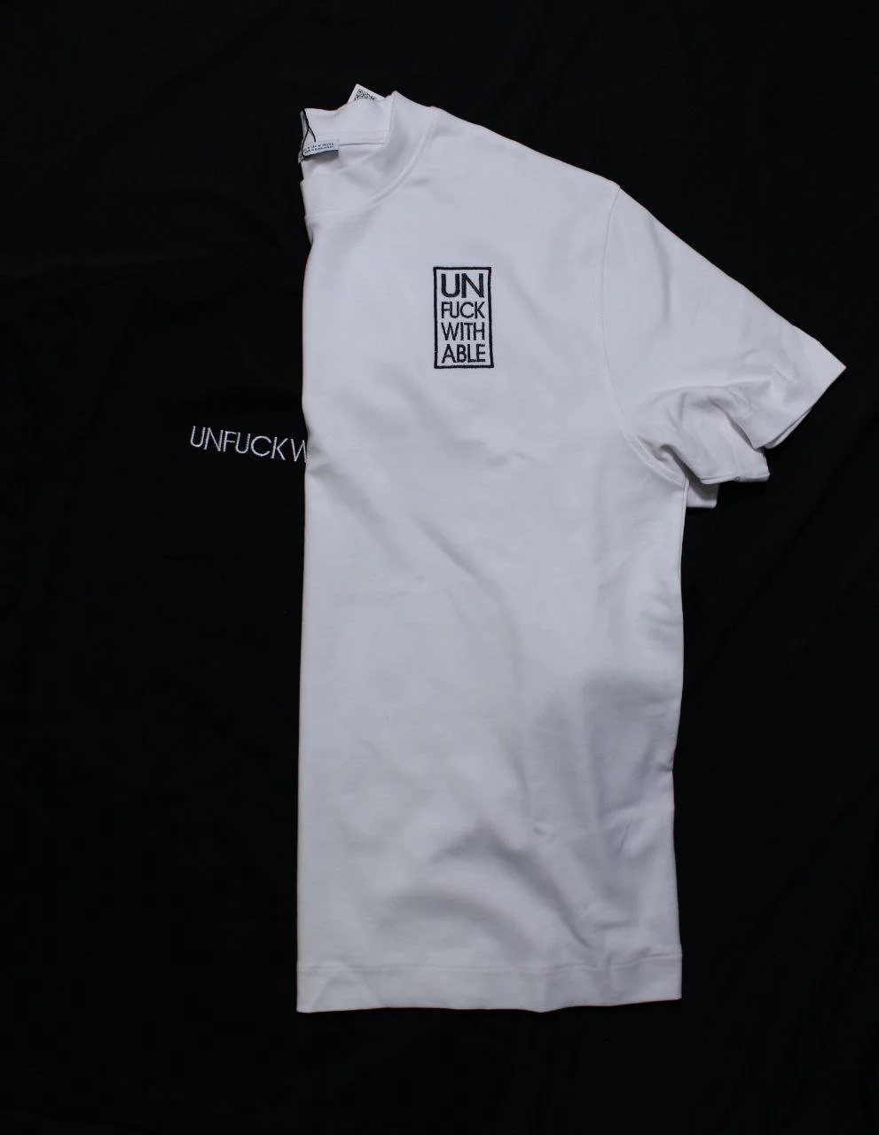 Maglietta bianca con scritta nera 'UNFUCKWITHABLE' in un quadro.