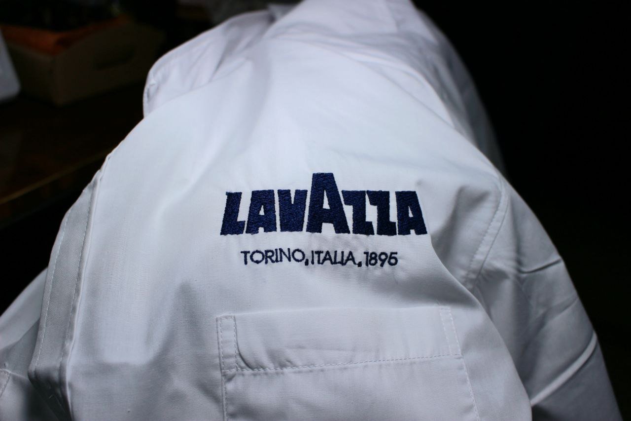 Giacca bianca con il logo e il testo 'LA VAZZA' e 'TORINO, ITALIA, 1896' ricamati in blu sul retro.