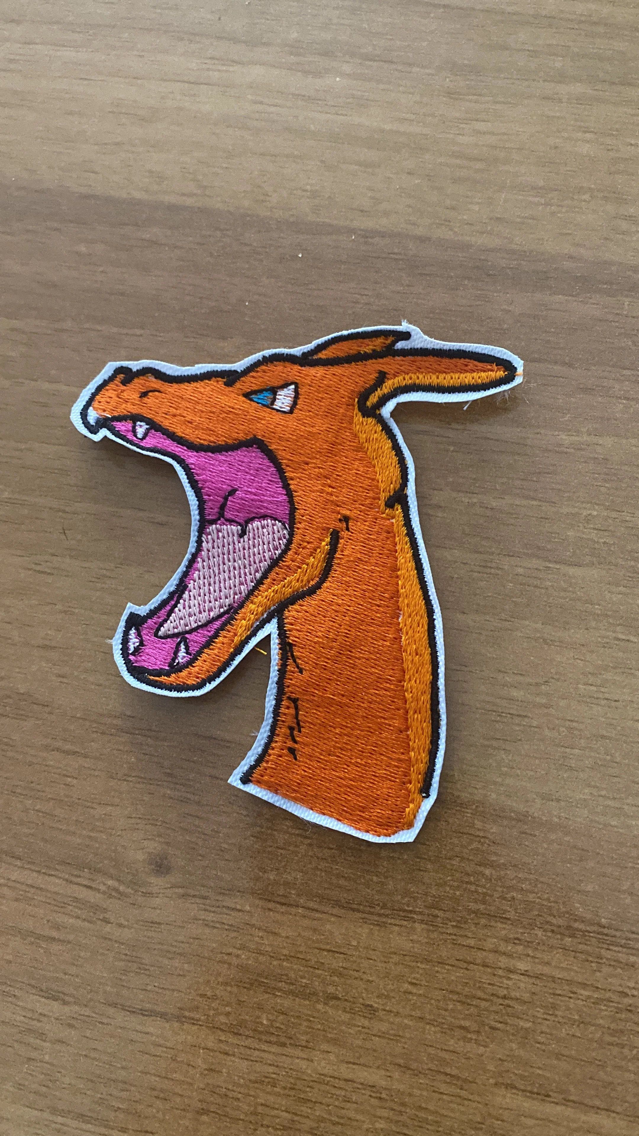 Applicazione ricamata di un lombrico arancione con bocca grande aperta, lingua rosa e denti