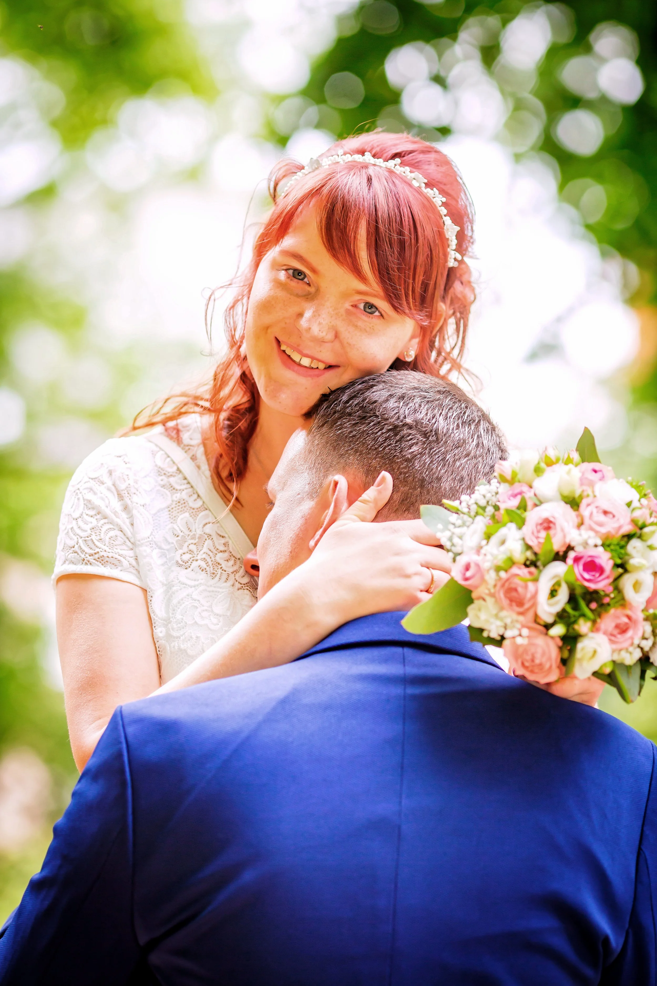 Ein lachendes Brautpaar bei einer Hochzeitsfeier im Freien, die Braut hält einen Blumenstrauß.