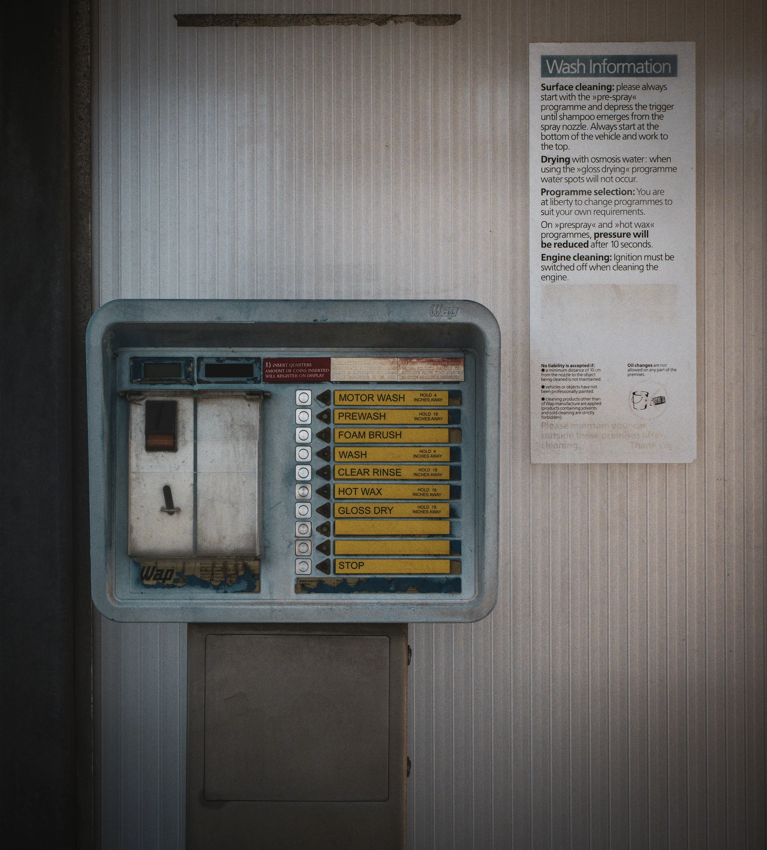 Automat für Autowaschanlage mit Programmauswahl und Anweisungen zur Nutzung. Enthält Optionen wie Motorwäsche, Vorwäsche, Schaumbürste, Reinigung, Klarspülen, Heißwachs und Glanztrocknung. Anweisungen sind auf einem Schild neben dem Automaten angebra