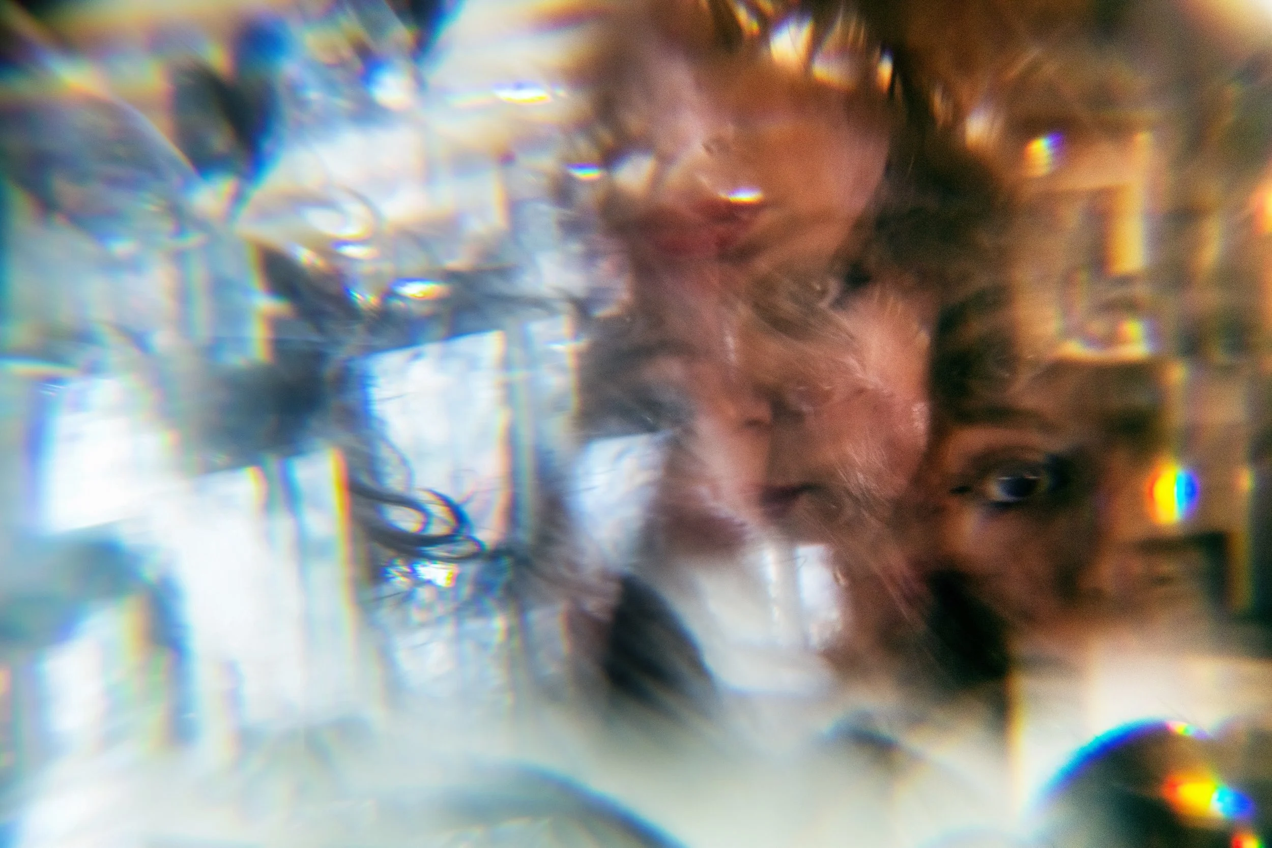 A woman with long wavy hair partially submerged in water with rainbow reflections and light distortions.