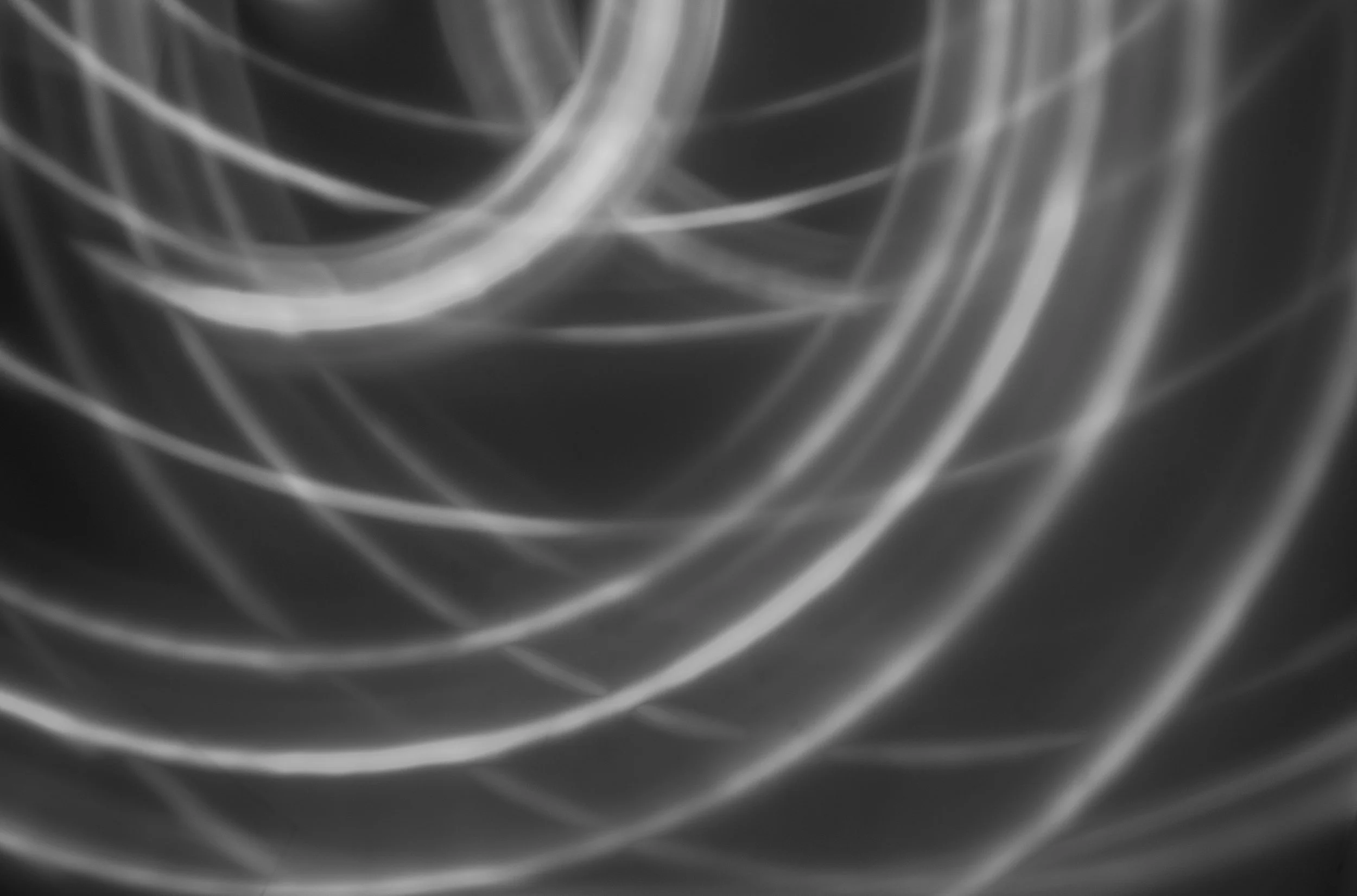 Black and white abstract image of swirling and curved light streaks forming a dynamic pattern.