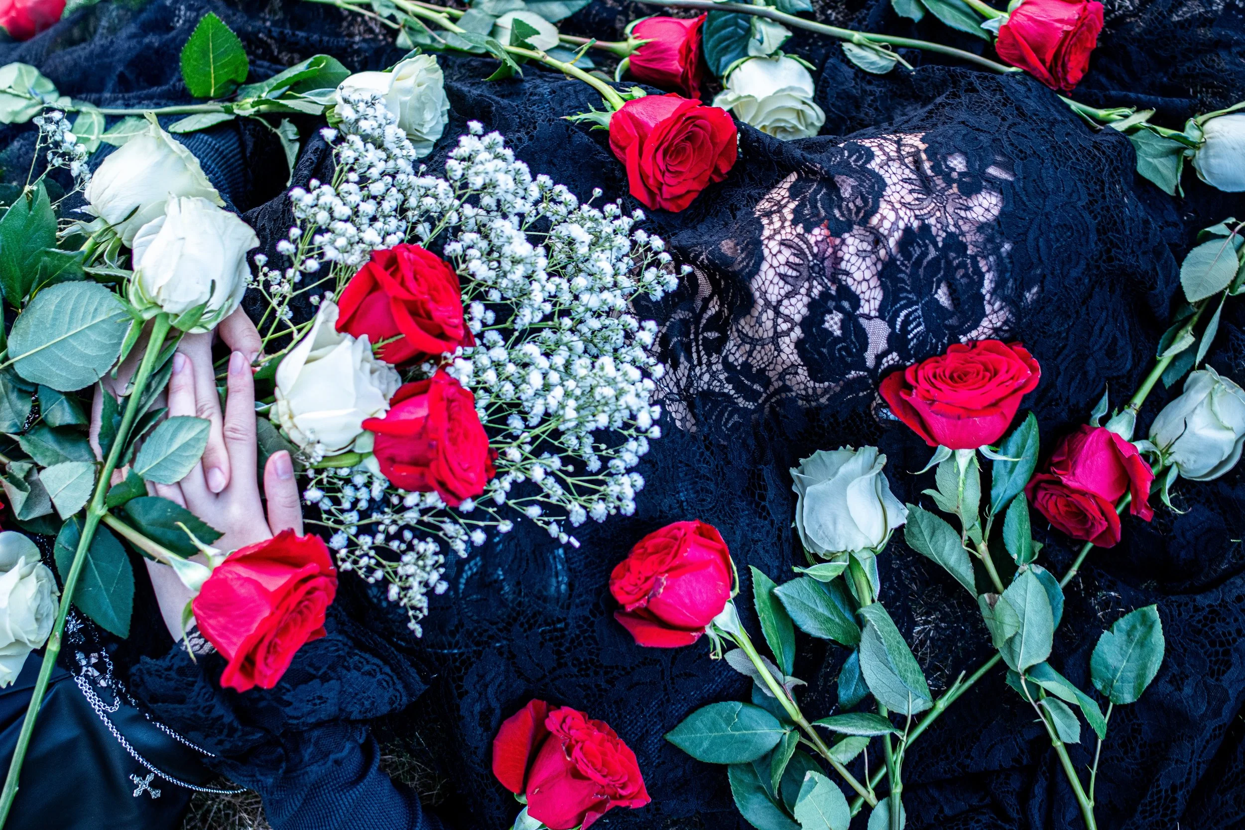 Flower arrangement with white, red, and pink roses, white carnations, and baby's breath on black lace fabric.