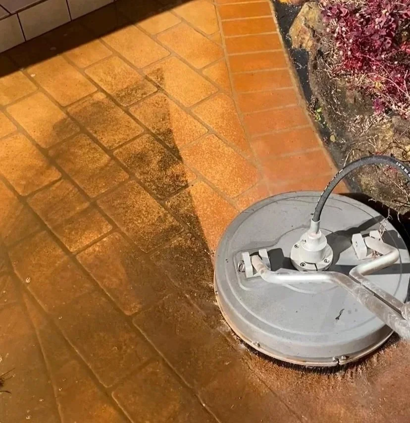 A floor buffer cleaning a tiled brick floor, creating a cleaner and darker area of tiles compared to the uncleaned area.