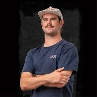 Mann in blauer T-Shirt und Baseballcap, lächelnd, vor schwarzem Hintergrund
