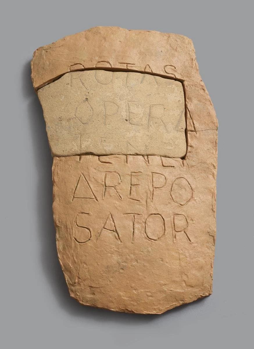 Ancient sandstone fragment with carved Greek inscriptions, some words visible include 'ARÉPO', 'SATOR', and other partially carved words.