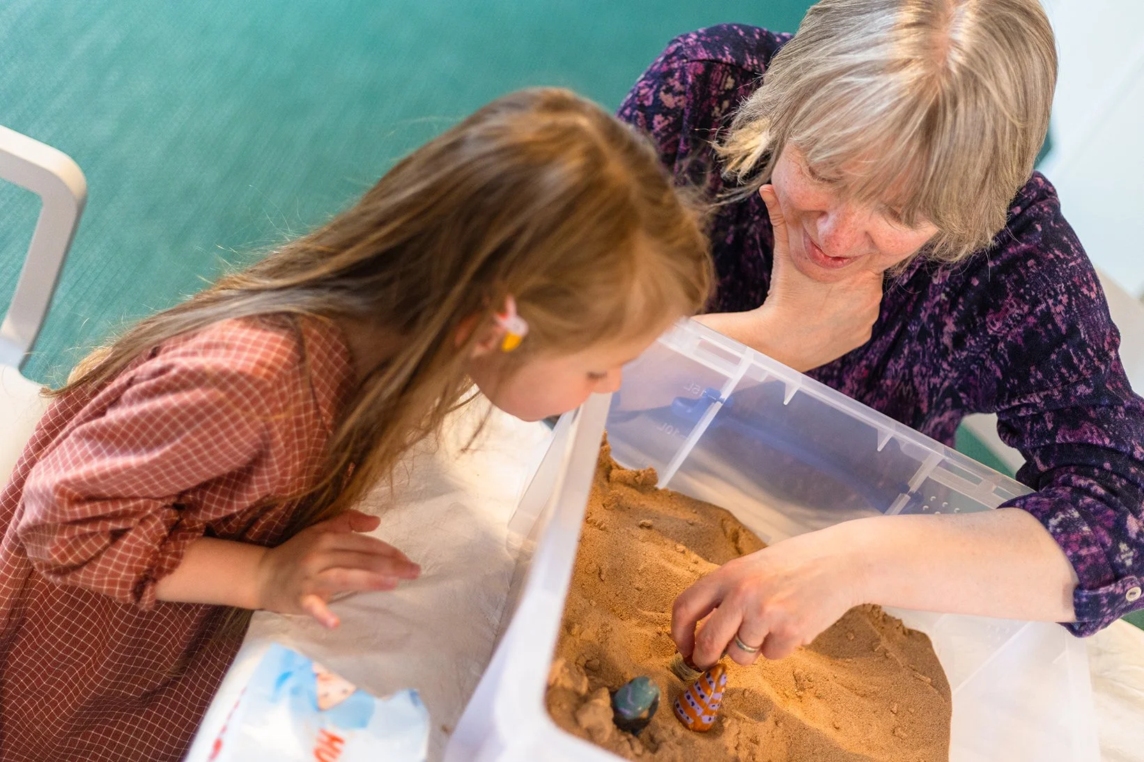 A young girl and an older woman observe and play with Dadikwakwa-kwa (shell dolls), created by the Anindilyakwa community, in a sandbox, as part of an event at Manchester Museum.